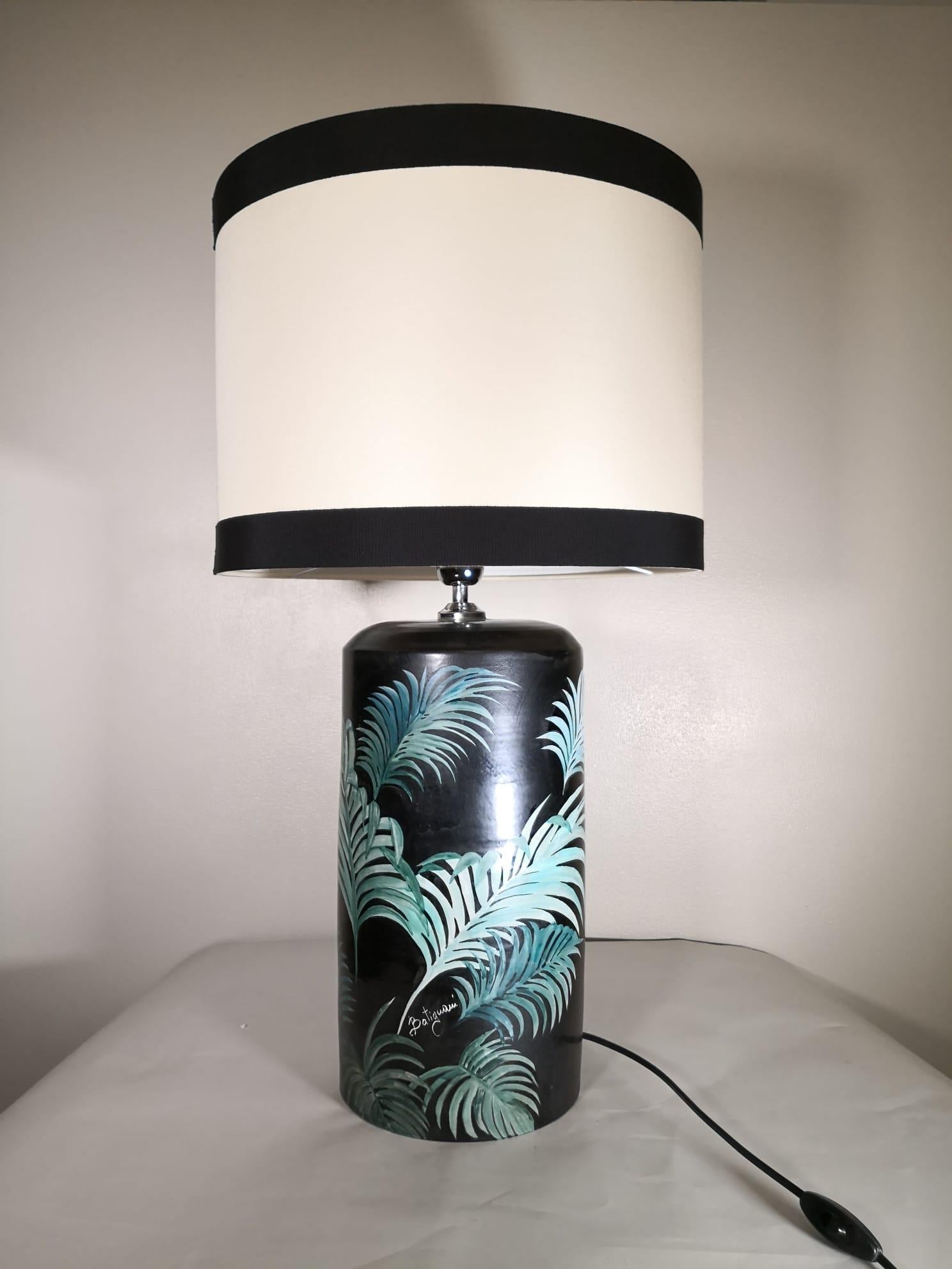 Colorful and exotic artisanal hand painted ceramic lamp portraiting palm leaves on a black background.
This lamp is entirely hand painted by the ceramists of the artisan company 