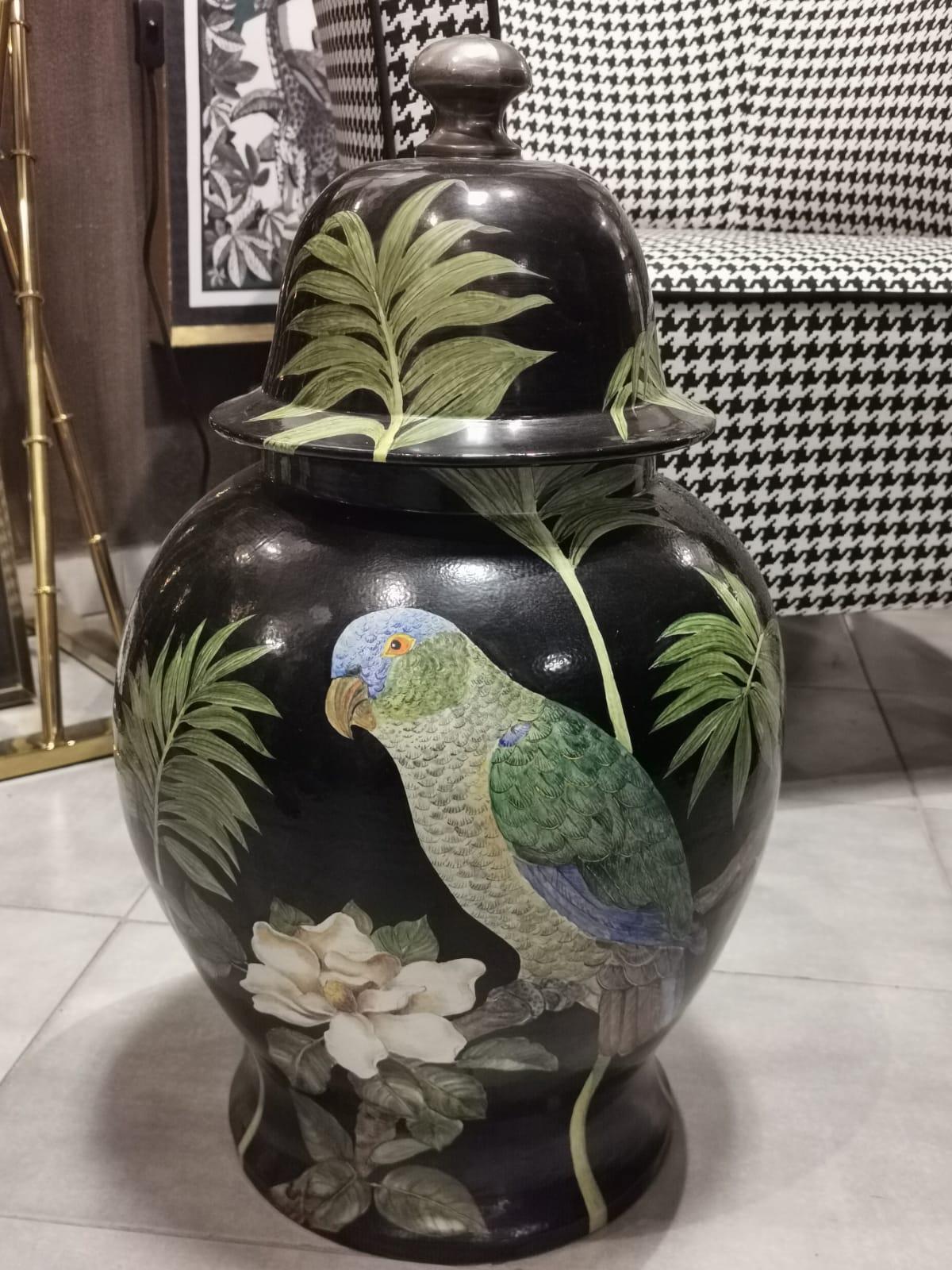 Colorful and exotic artisanal hand painted vase with lid portraiting a blue and green parrot and vegetation on black background. 
This vase is entirely hand painted by the ceramists of the artisan company 