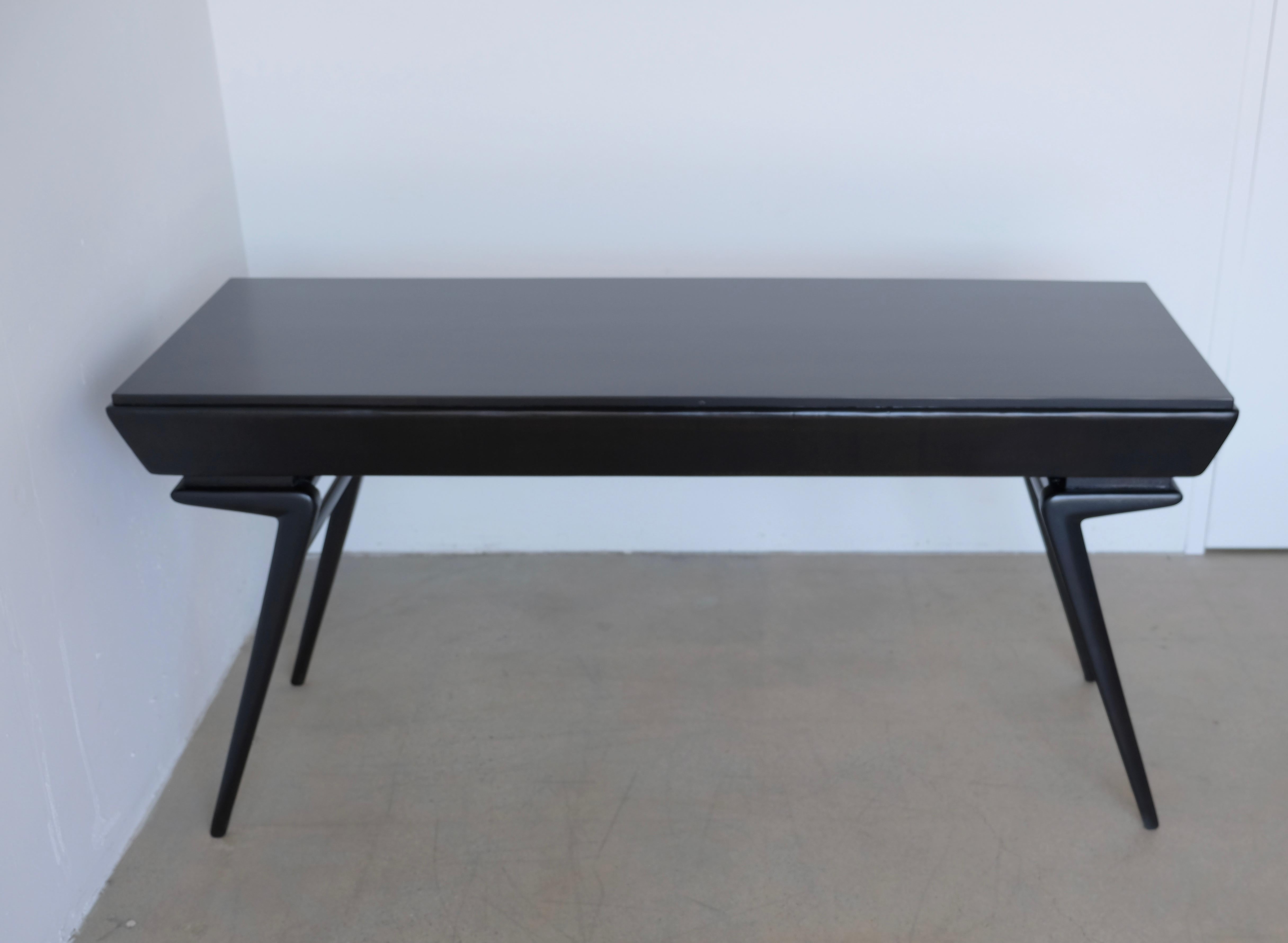 A handsome vintage desk that has been freshly ebonized with a beautiful black stain that allows a bit of the wood grain to show through. The top of the desk is a laminate type material. The desk has angled legs reminiscent of the work of Ico Parisi.