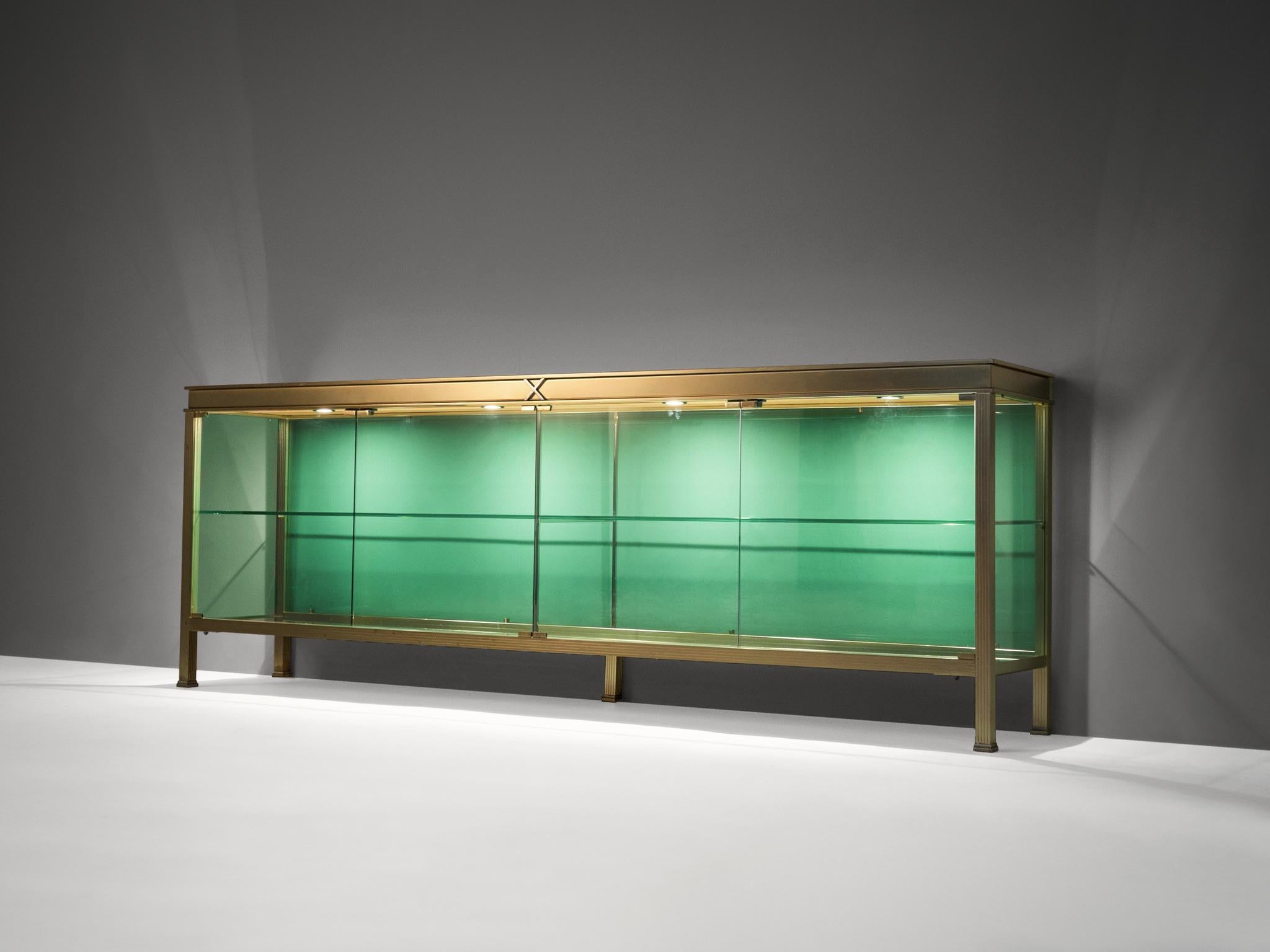 Vitrine, brass, metal, glass, Italy, 1960s. 

This luxurious 'aquarium' vitrine is made of brass and the two sliding doors are executed in colored green glass. Its open construction provides a fragile yet elegant and open look. Illuminated with