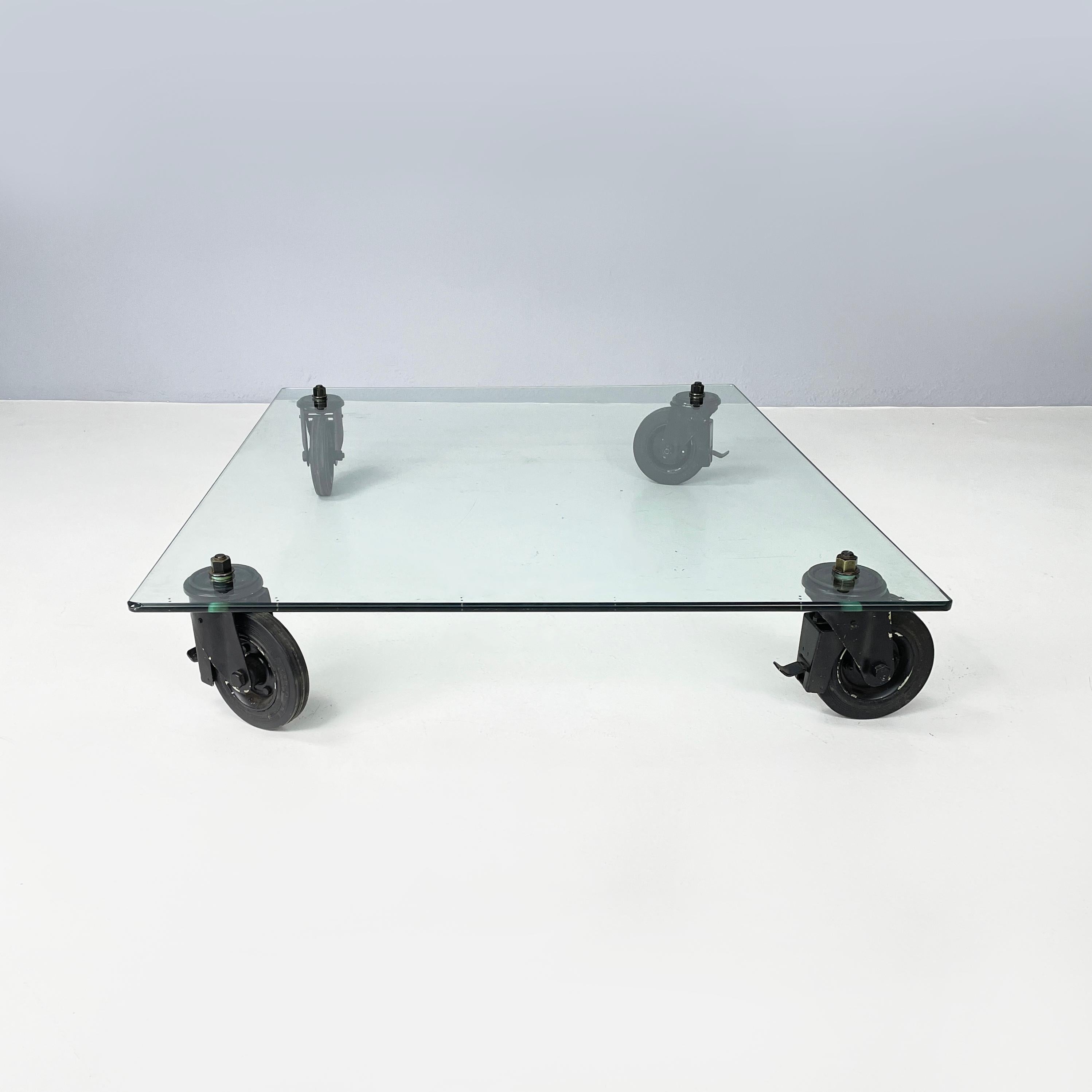 Italian industrial modern Glass coffee table by Gae Aulenti for Fontana Arte, 1980s
Coffee table with thick rectangular glass top. The 4 legs, fixed to the glass with large screws, are 4 rubber and black metal wheels, which allow the table to be