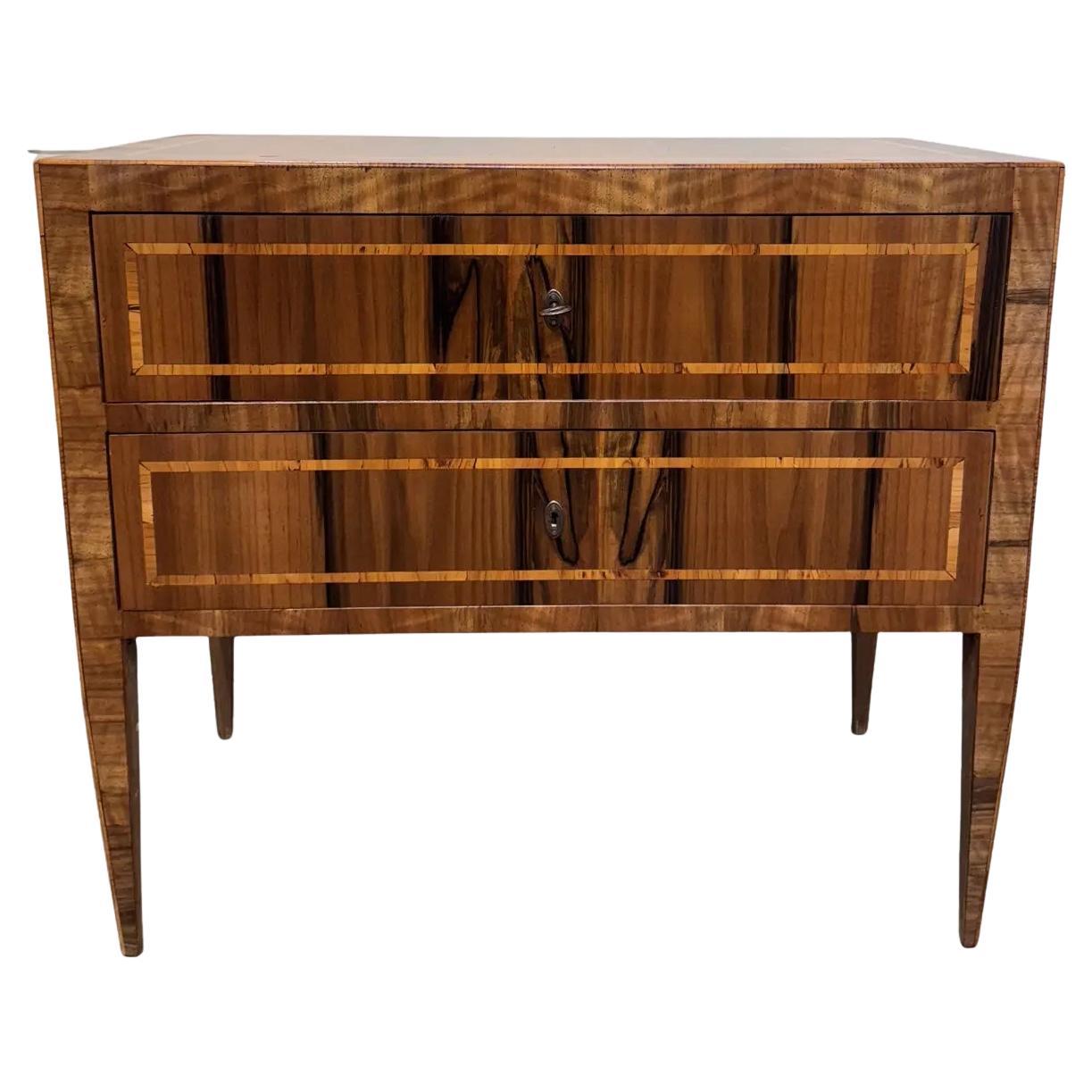 This stunning Italian veneer commode side table exudes timeless elegance with each chest featuring intricate wood inlays, showcasing exquisite artistry and attention to detail. The rich tones of the wood are beautifully complemented by the