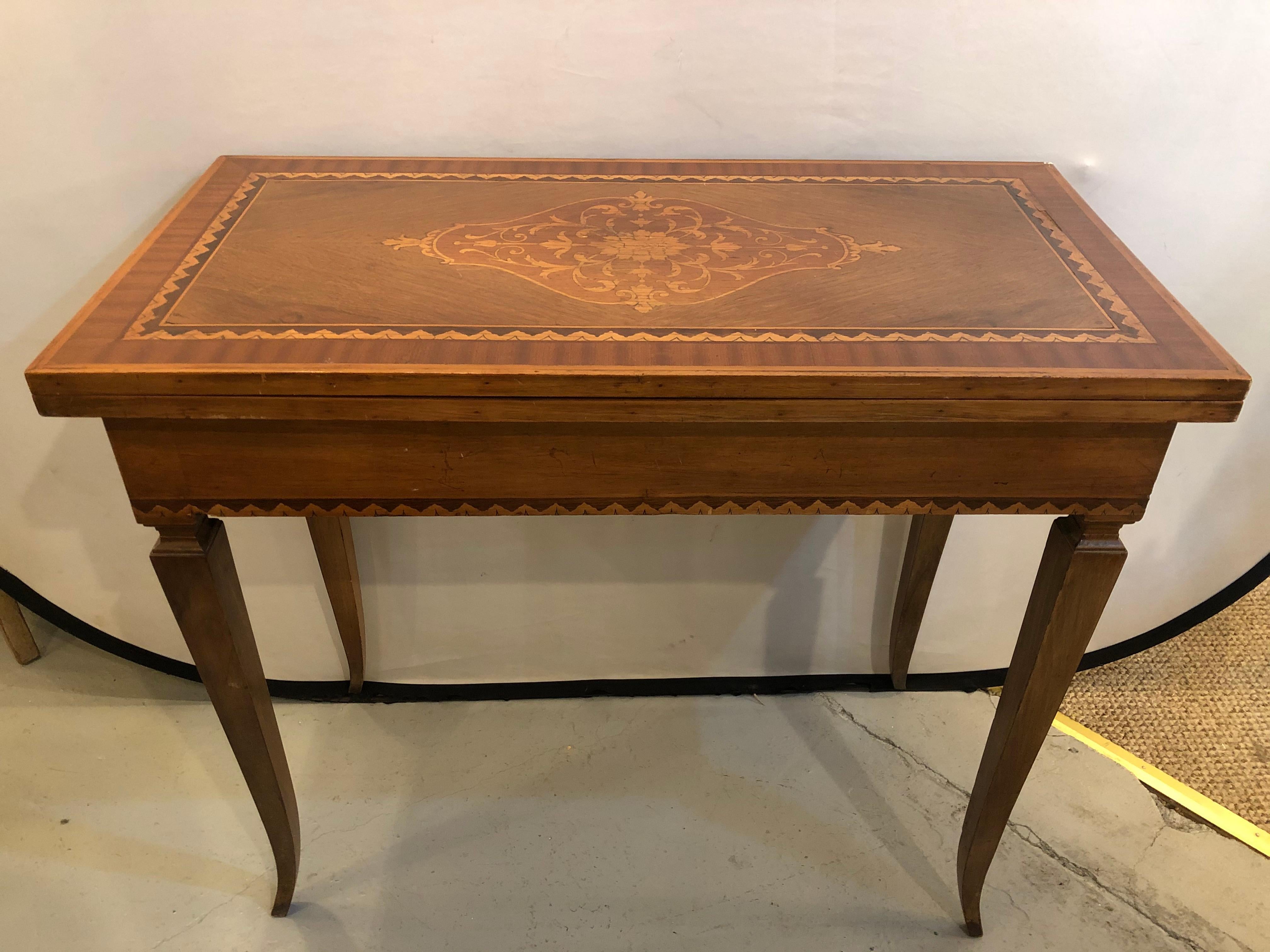 Italian inlaid folding game or card table. This finely inlaid circa 1920s game or card flip top table is wonderfully inlaid. The top on curved tapering legs leading to an inlaid border apron supporting a flip tabletop that can ope to sit four