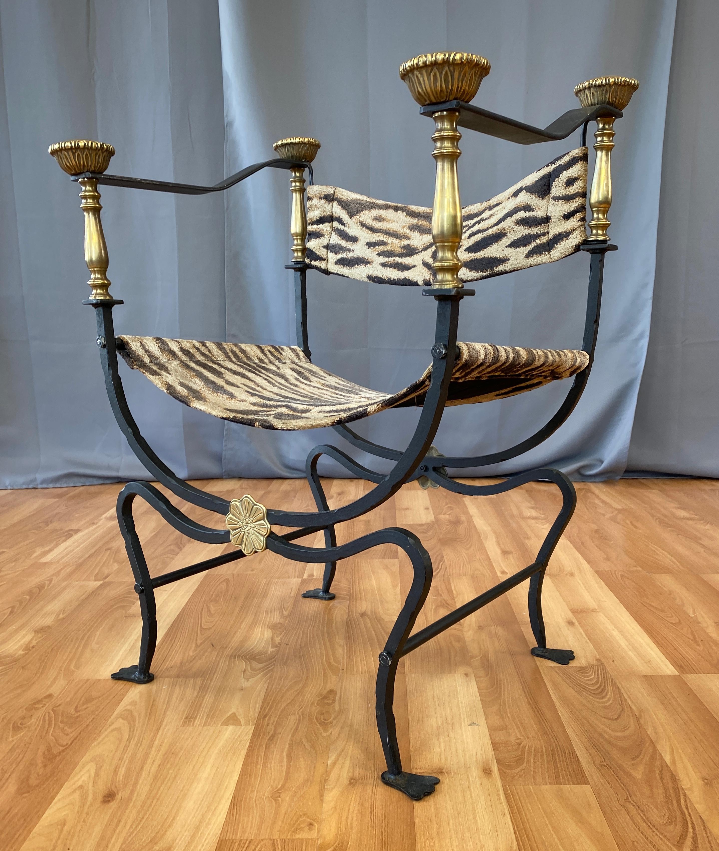 Iron and brass Savonarola style chair, circa 1950s-1960s.
Wrought iron, with brass detailing from the flower medallions on the x bracing up to the crown finials on the arms.
Then you have the whimsical tiger pattern upholstery for the sling seat and
