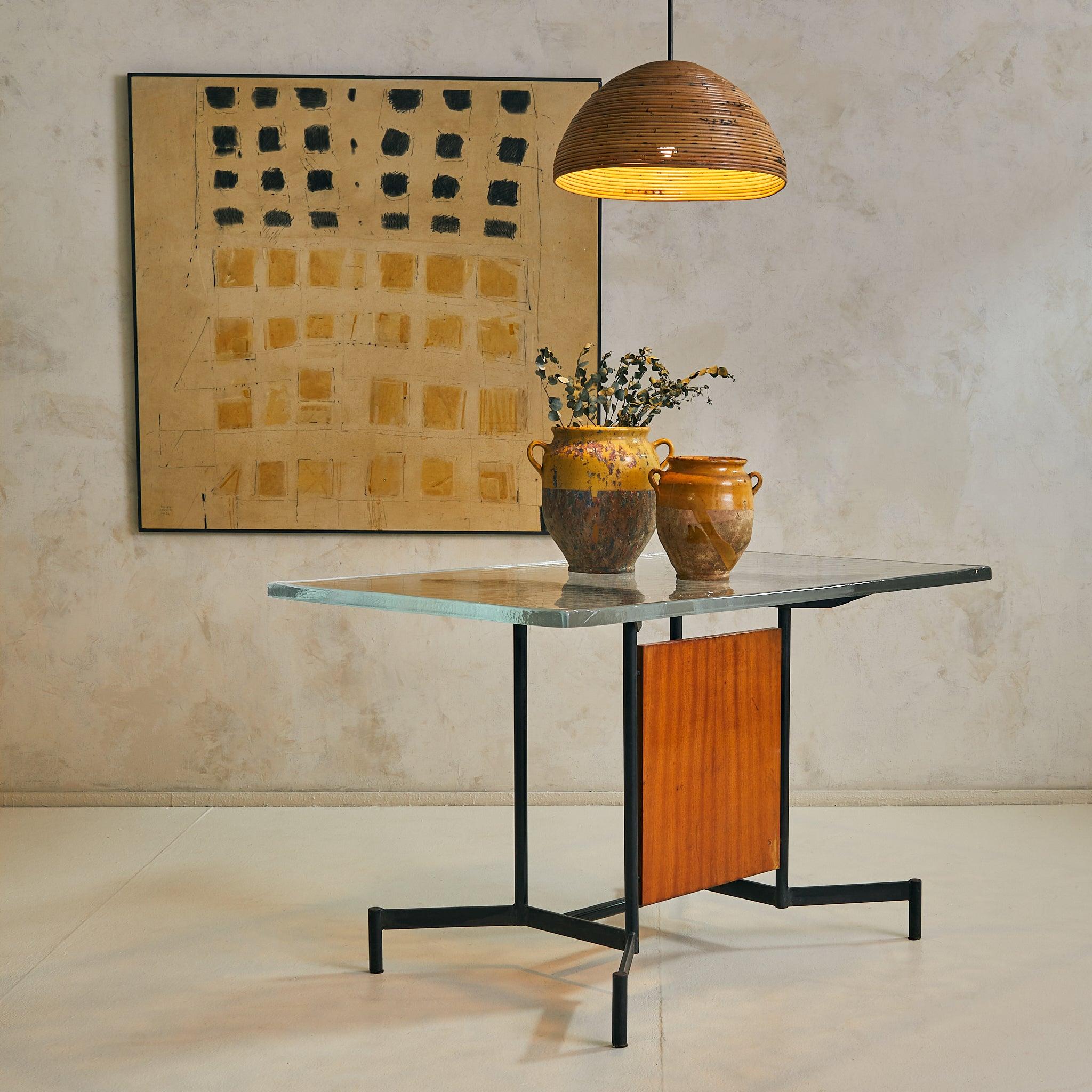 A 1950s Italian desk or console with architectural lines and a grounded presence. The iron base flares outward in a winged silhouette—sharp angles offset by a warm, inset wood panel. A rectangular pane of cast glass—1.25