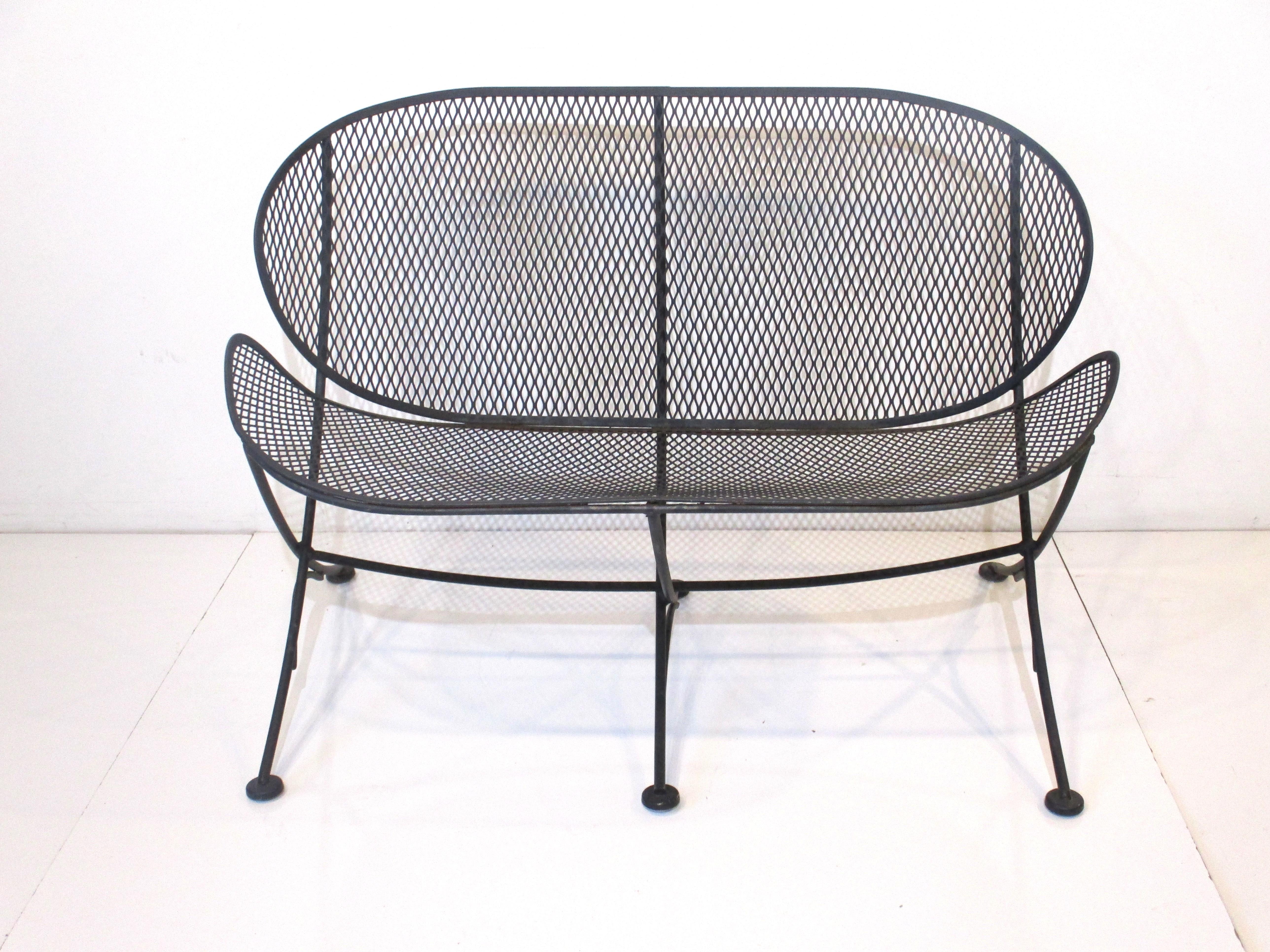 A sculptural iron and mesh orange slice loveseat in a flat black finish with curved legs having foot pads making the piece very stable. A great design for your garden, deck or three seasons room designed by Maurizio Tempestini for John Salterini
