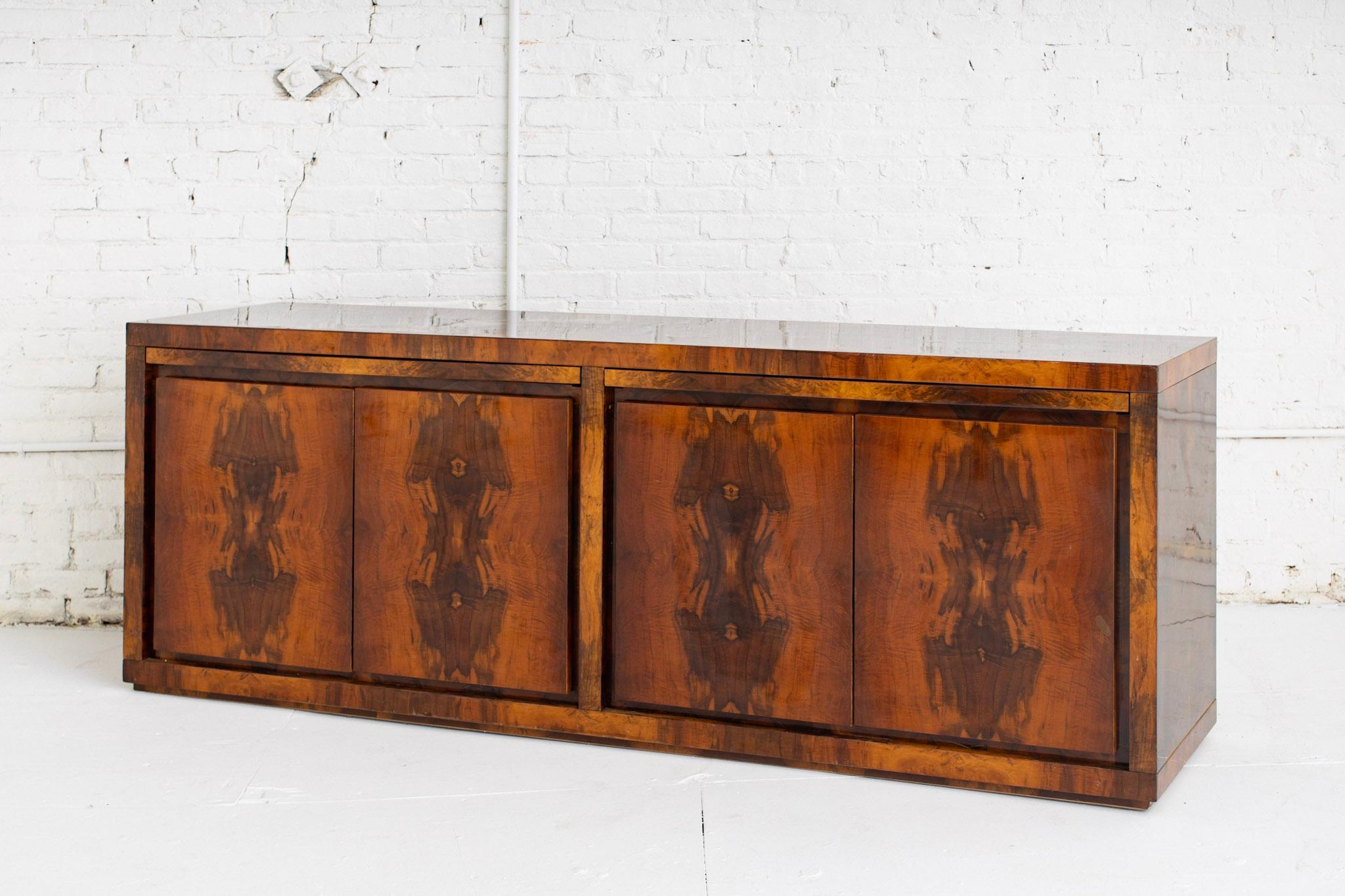 High gloss lacquered walnut burr / burl credenza. Rich grain detail creates a book-matched surface pattern throughout. 3 cabinet doors open to inner shelves. One cabinet door opens to 4 inner drawers. 2 upper extendable work / serving areas. Sourced