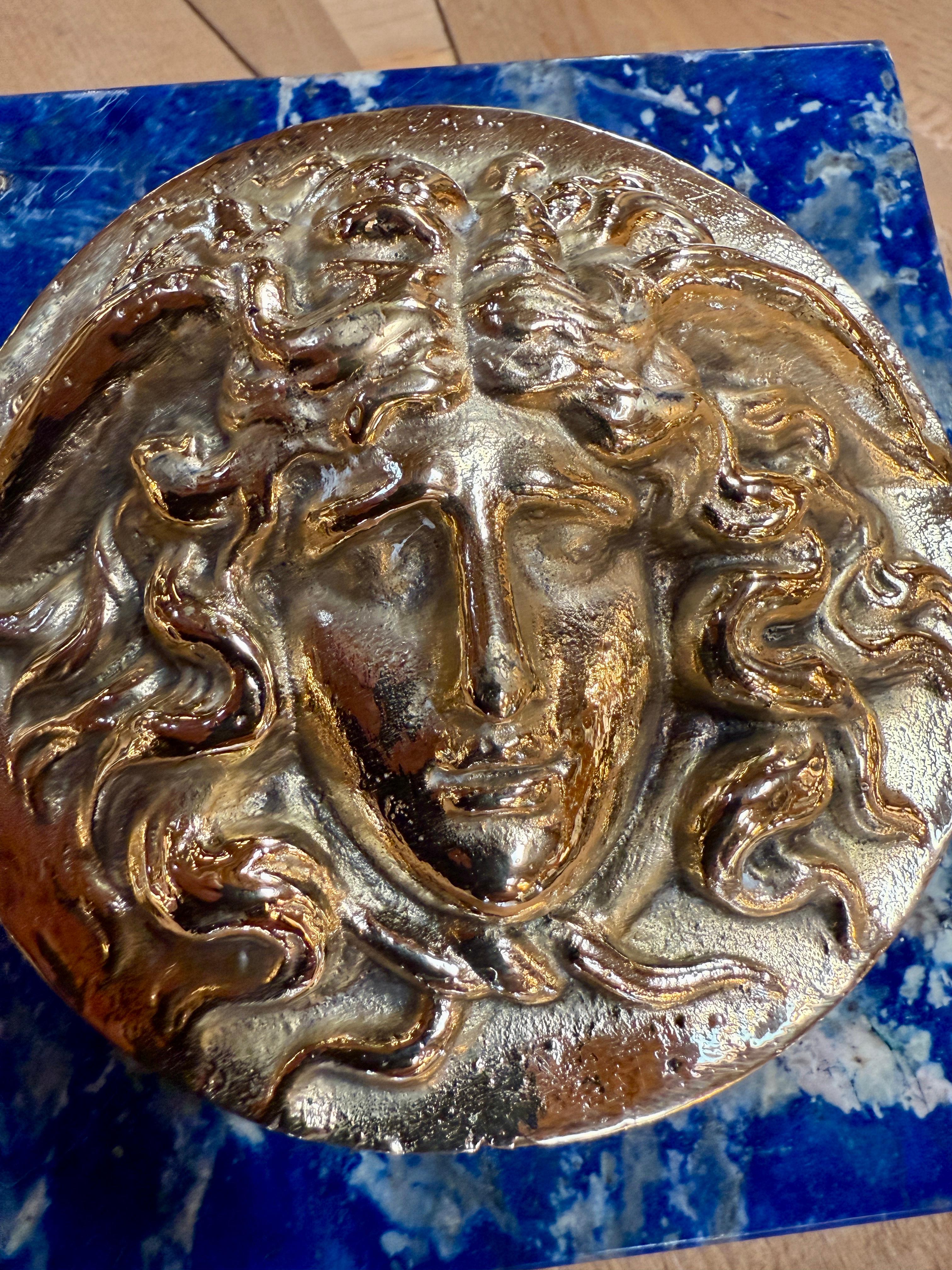 Questa straordinaria targa italiana combina la profonda e vivida bellezza del lapislazzuli naturale con la raffinata eleganza del bronzo dorato. Al centro, una testa di Medusa finemente dettagliata emerge in alto rilievo, simboleggiando forza e