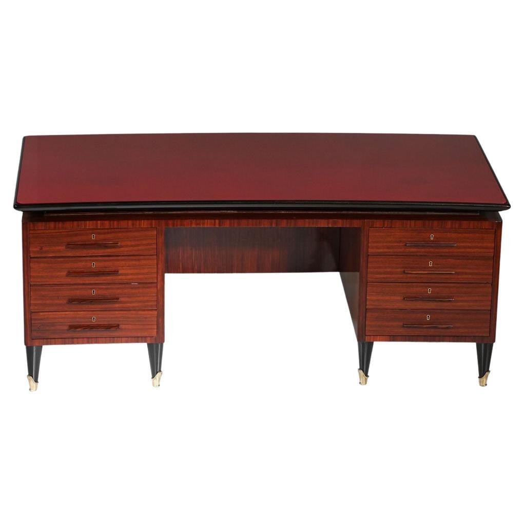 Imposanter Schreibtisch aus den 50er und 60er Jahren, der dem italienischen Designer Vittorio Dassi zugeschrieben wird. Struktur aus Massivholz und Furnier, Platte aus rotem Glas. Er besteht aus zwei Kästen mit je 4 Schubladen auf jeder Seite. Sehr