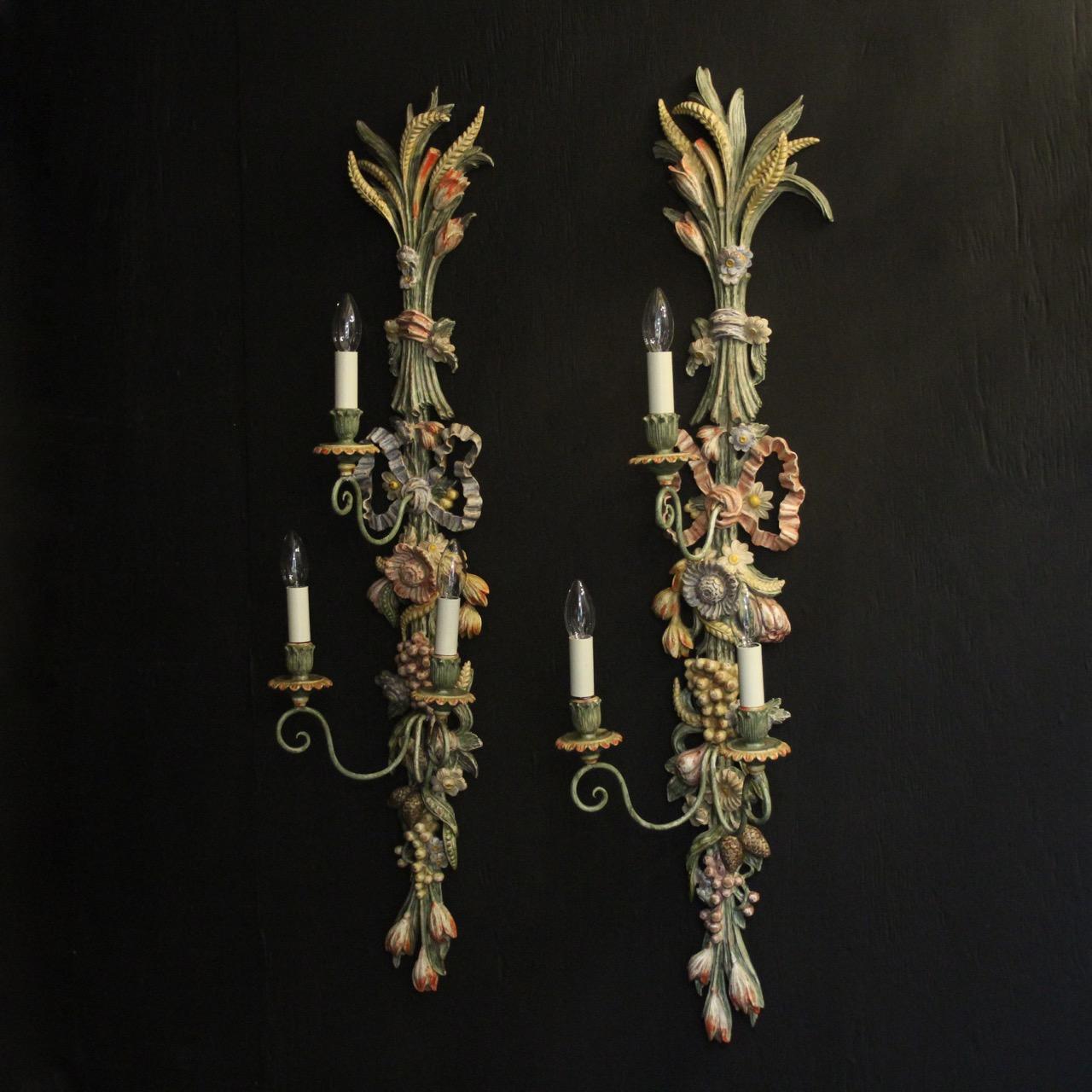 A Large pair of decorative Italian polychrome painted carved wood triple arm tiered wall lights, the simple scrolling arms with carved wooden candle sconces, issuing from a ornately carved pierced decorative floral and ribbon clad backplate, lovely