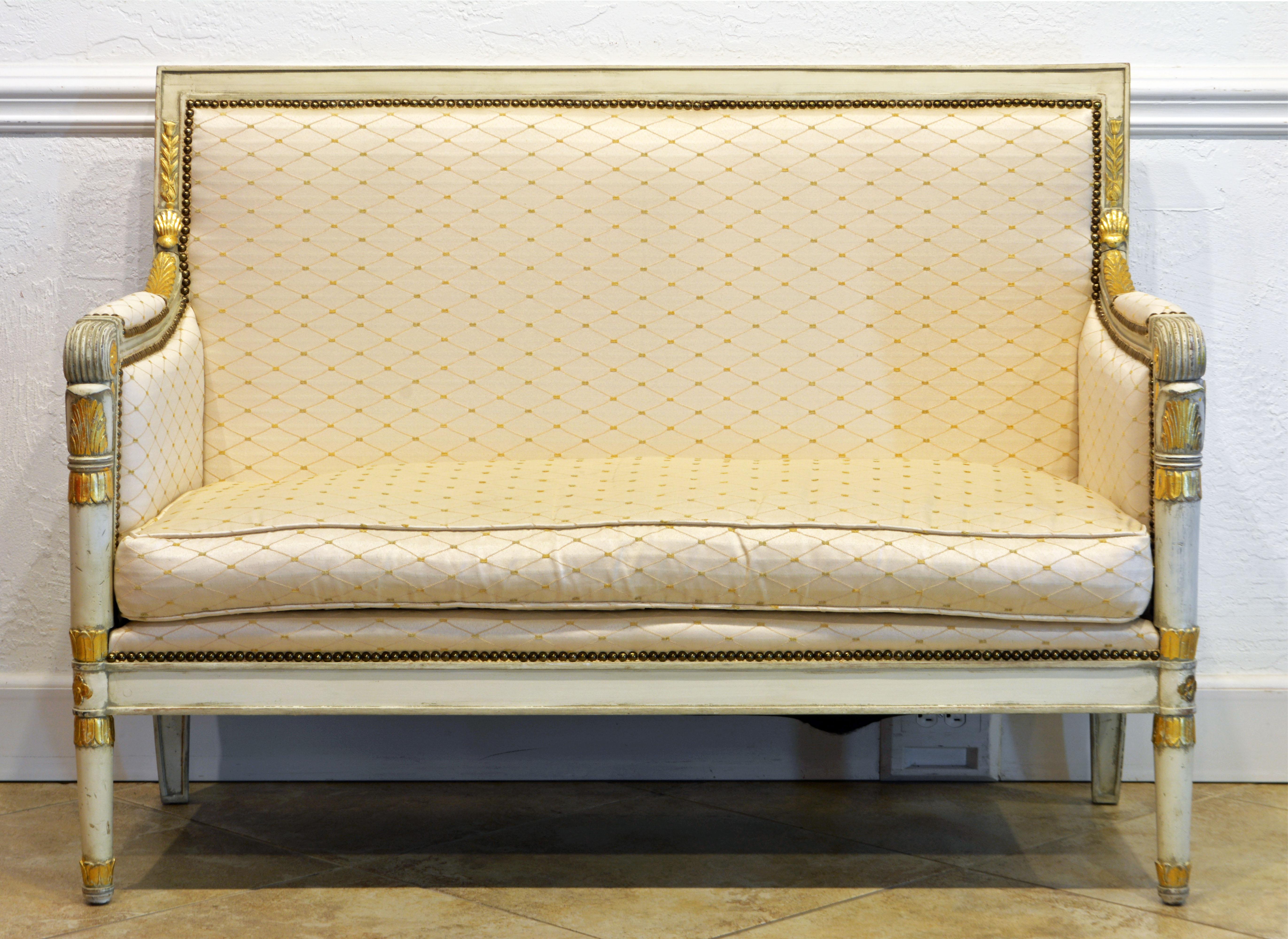 This neoclassical style Italian carved ivory white painted and parcel gilt settee features a frame carved with gilt leaves and rosettes accenting the painted parts in a highly attractive way. The cream colored satin cover compliments the elegance of