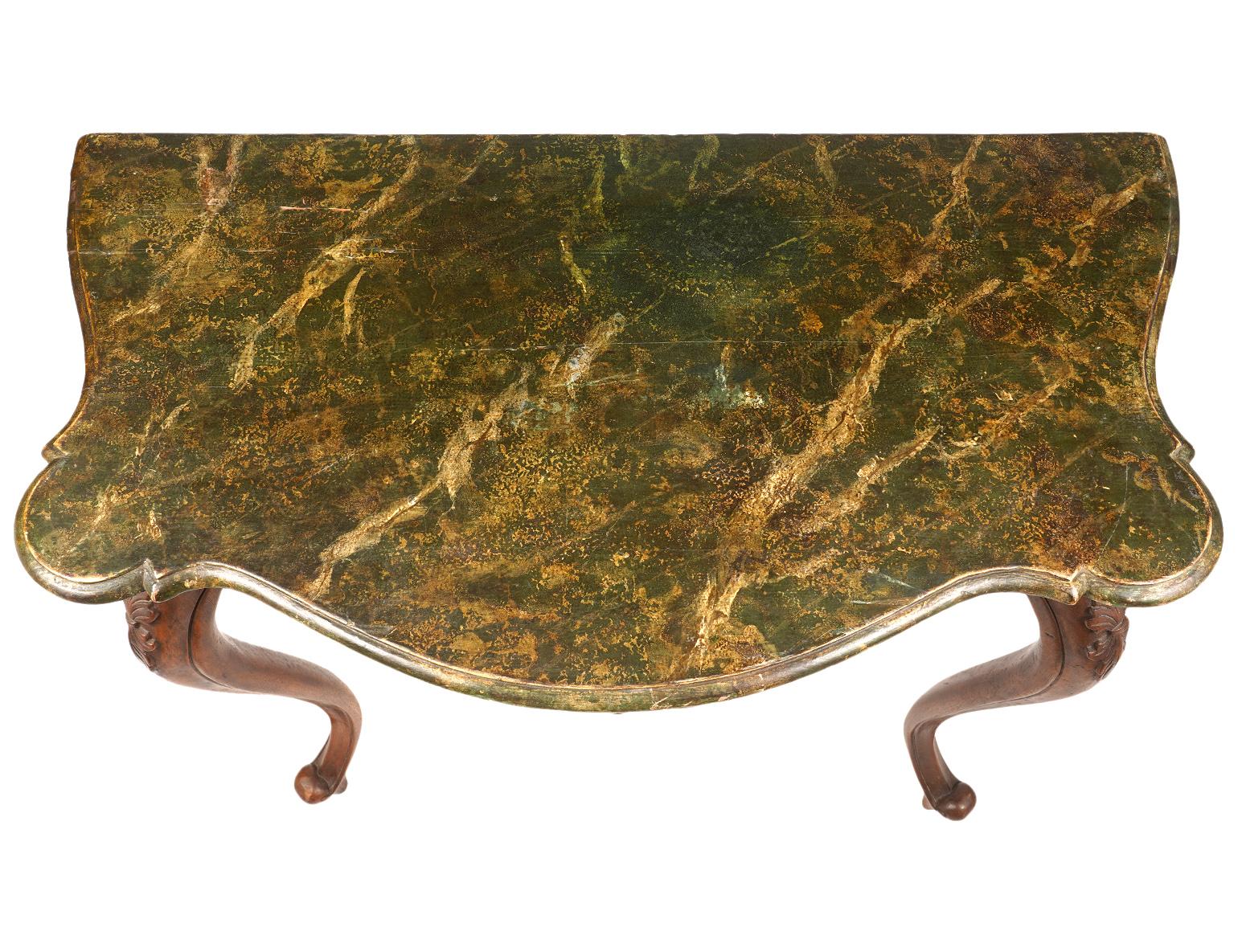 Resting on four boldly carved cabriole legs, the rear legs turned sideways, this Italian walnut console table, dating to the late 19th century, features a marbleized painted top above shaped aprons centering carved shells and scrolls on three sides.