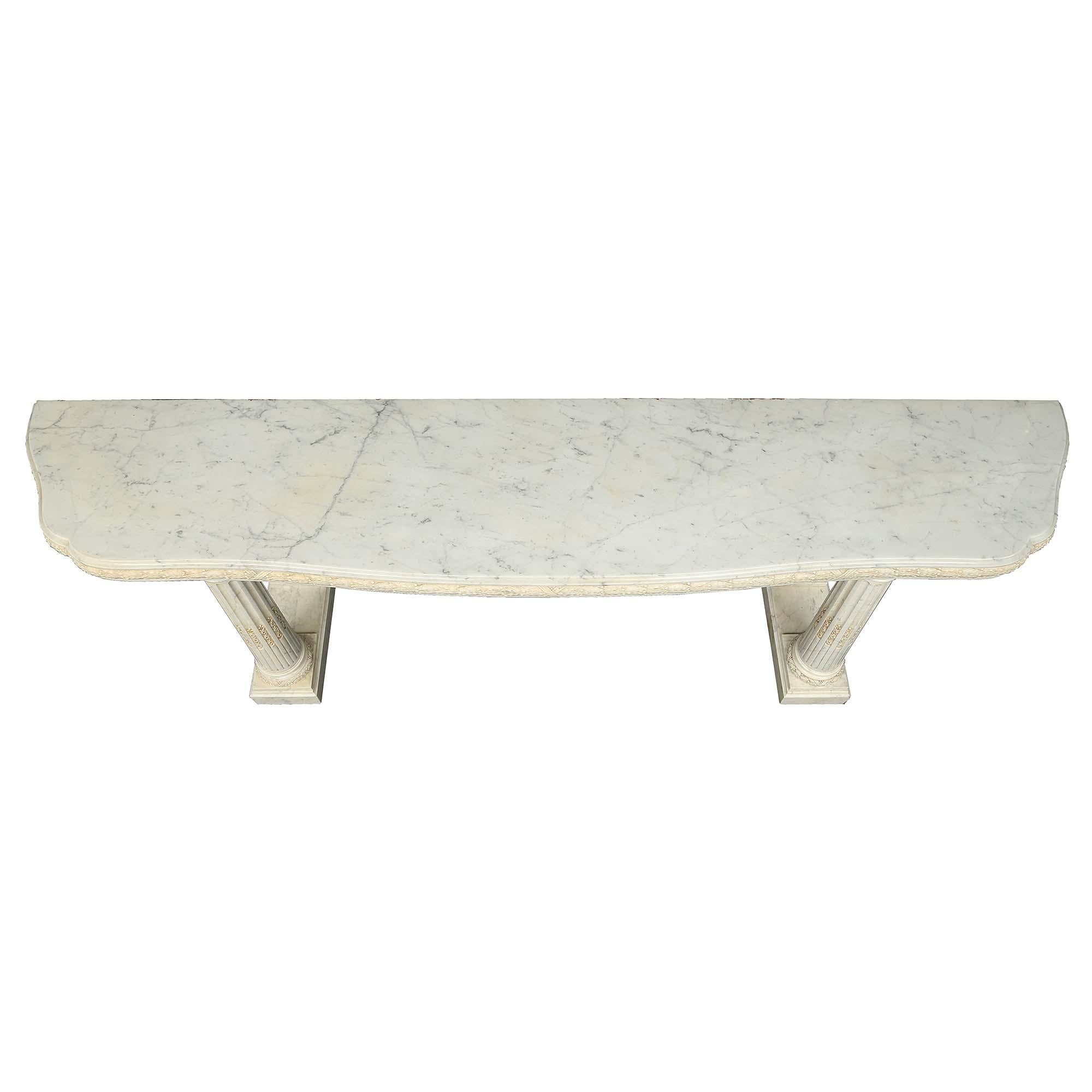 A magnificent Italian late 19th century white Carrara marble console. The console is raised on two rectangular plinths with four impressive fluted columns, with laurel tied wreath bases, finely carved foliate chandelles, and Les Oves designed top