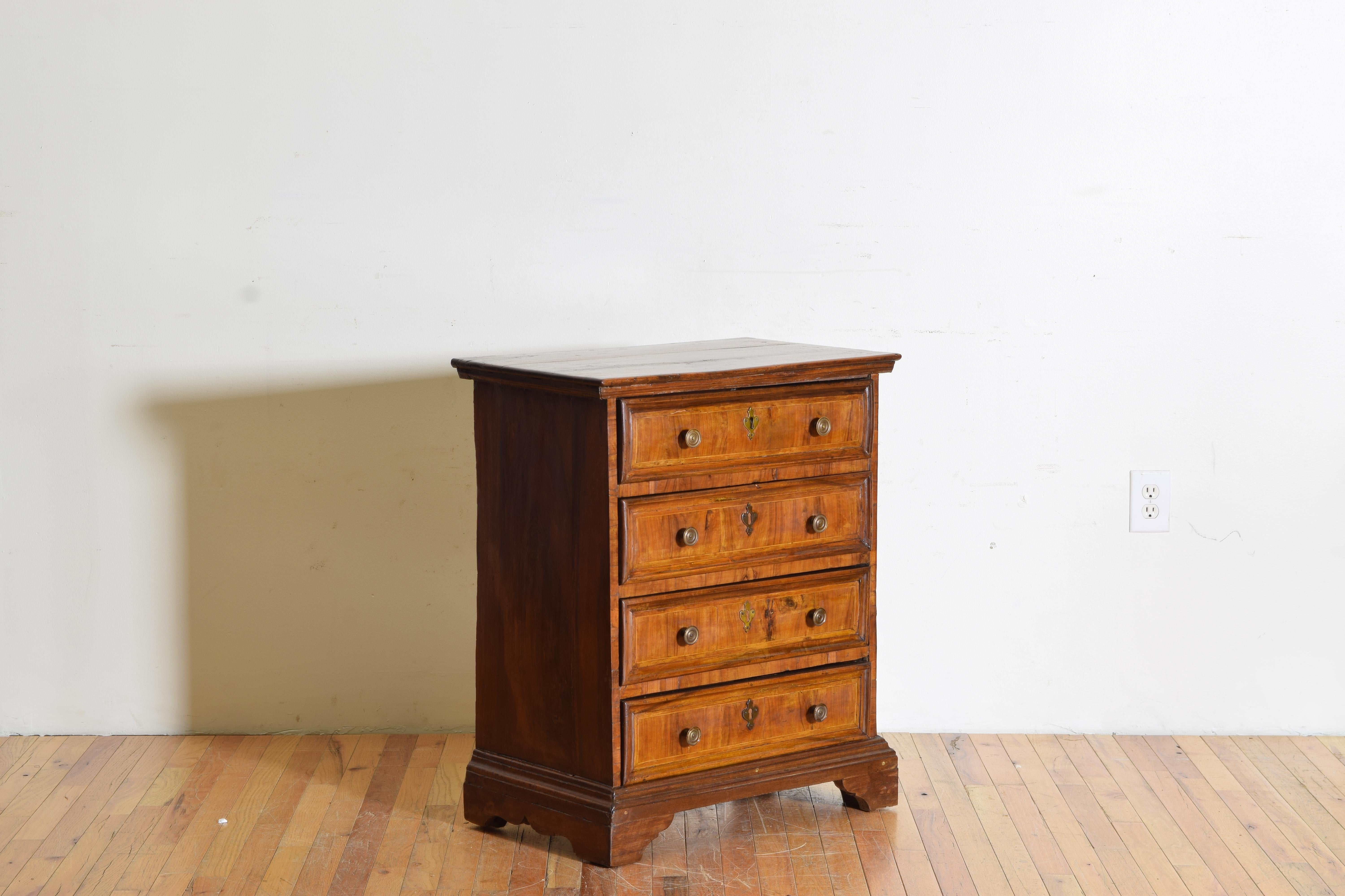 Having a rectangular top with small apron atop a case housing four drawers with antique patinated brass pulls, the case and drawers covered in thick walnut veneers with band inlays, raised on bracket feet.