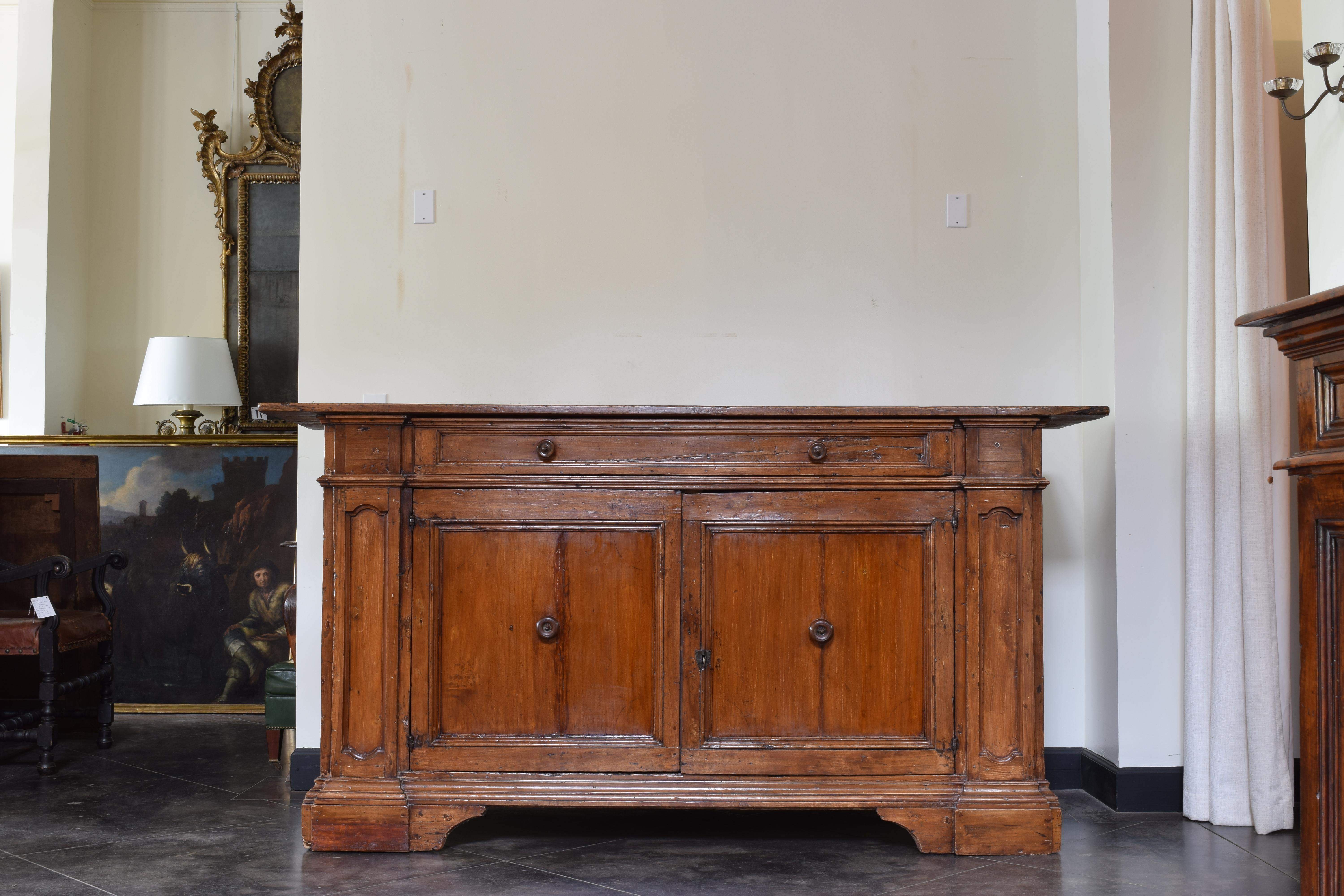 Likely Tuscan this larger scale credenza has a rectangular top above a conforming case housing one large drawer over a pair of paneled doors between recessed paneled pilasters, the interior upholstered, raised on large bracket feet, retaining turned