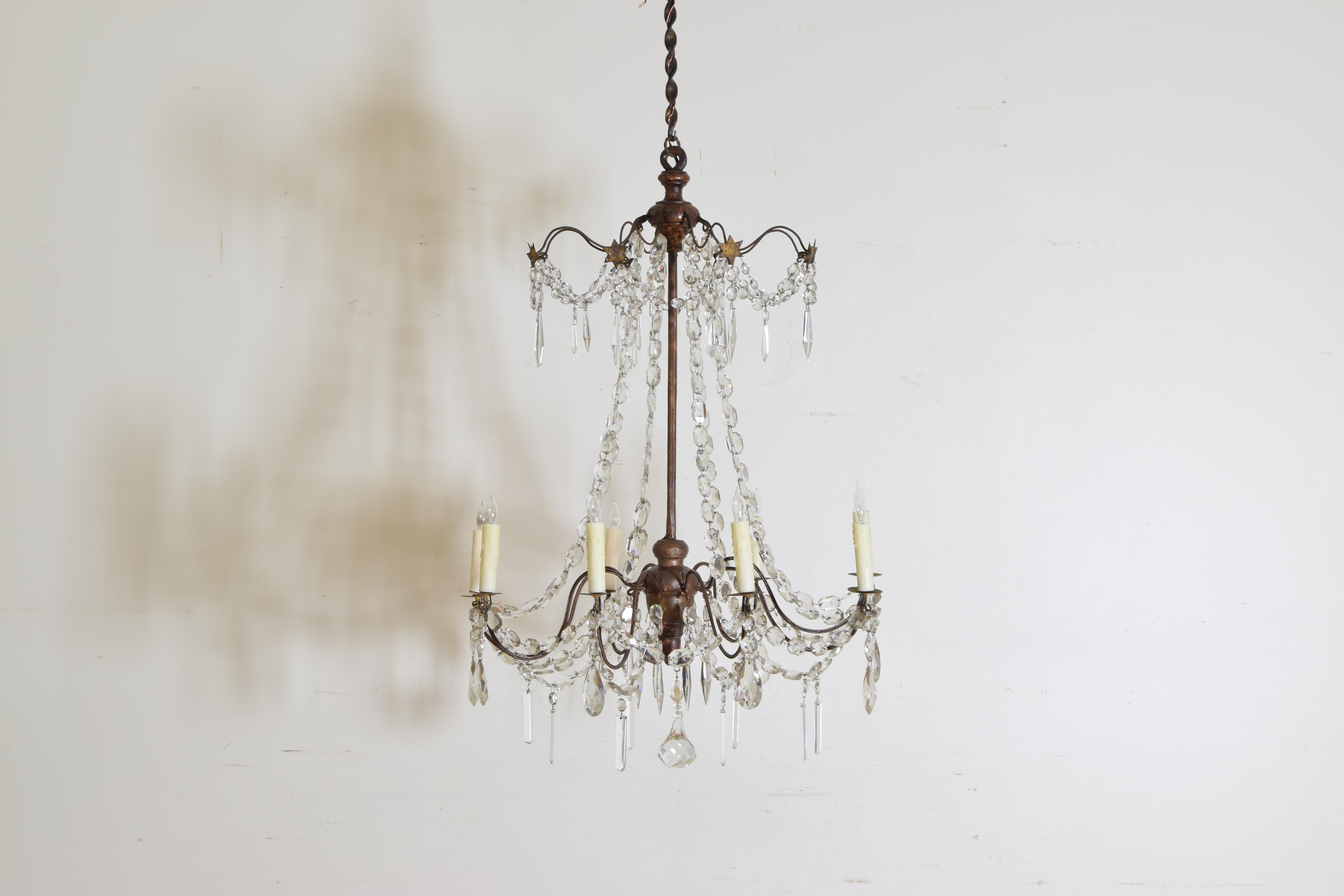 This chandelier is based upon a central wrought iron rod with turned a turned giltwood top and bottom, the top portion with gilt metal stars, both issuing thin iron arms with metal bobeches, the arms joined by glass prism chains, now wired