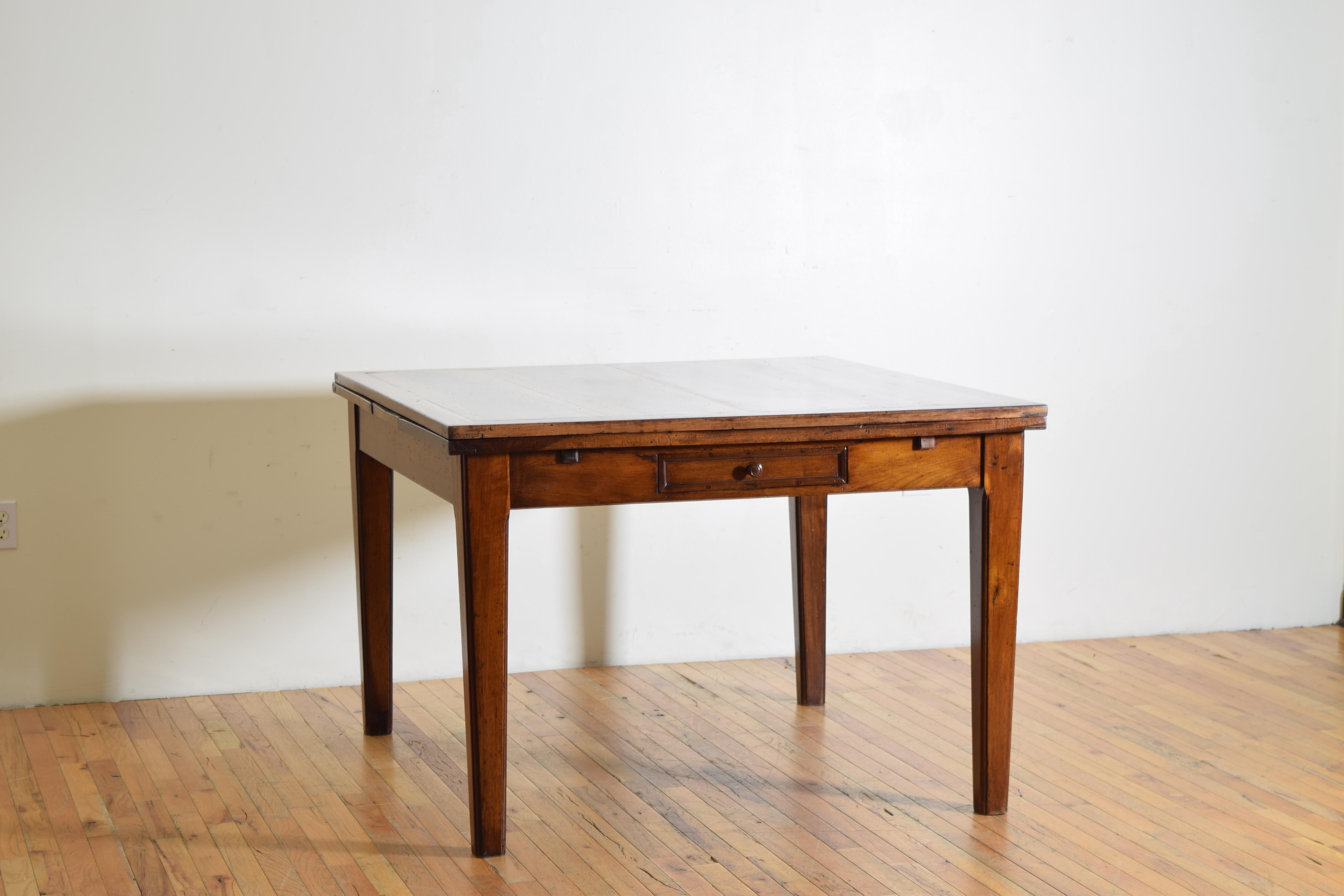 Almost certainly a kitchen table used for both work and meals, having a nearly square top with a lower level concealing two pull-out leaves transforming the table into a larger dining table, the apron housing one drawer, raised on square tapering