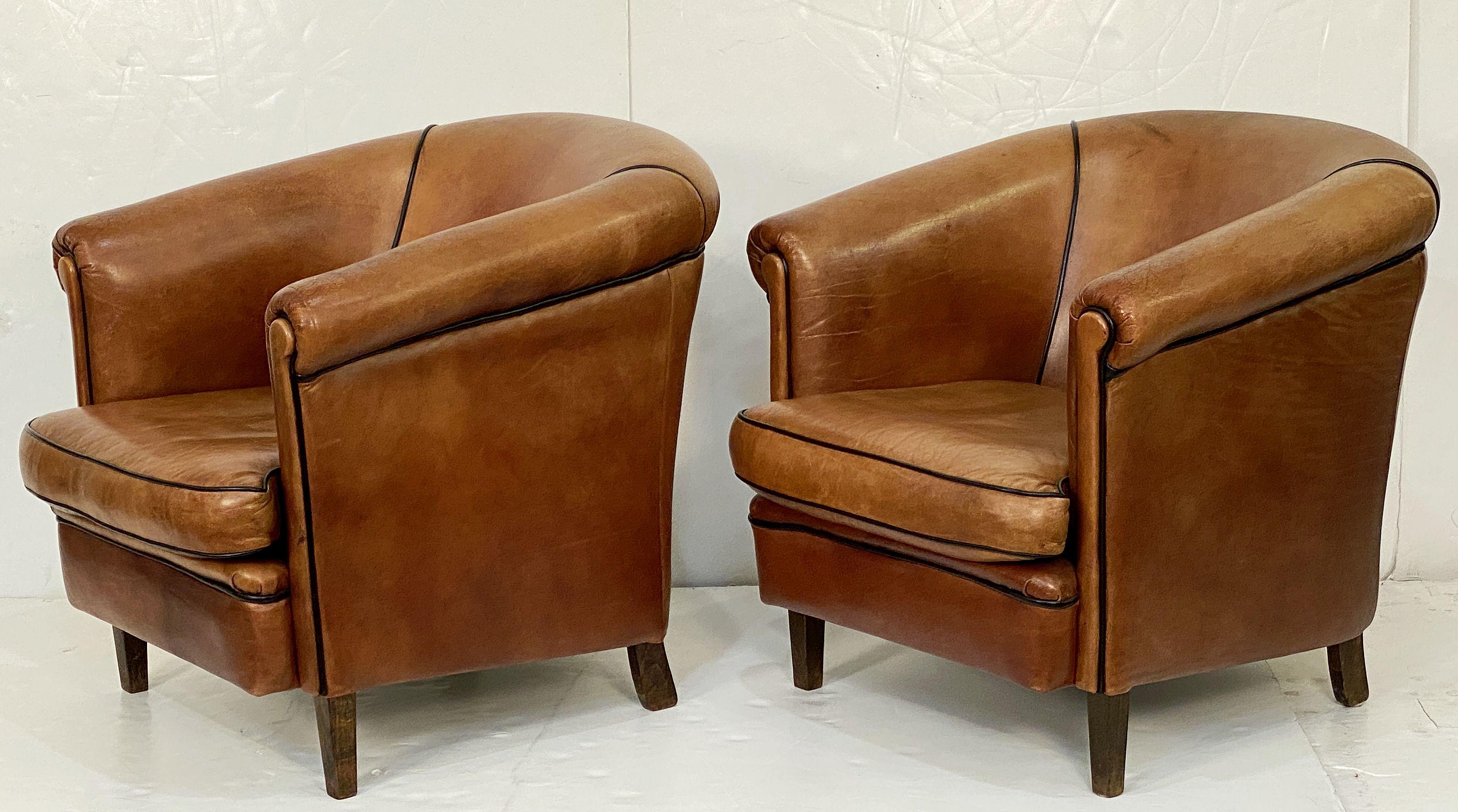 A pair of handsome period Italian leather upholstered club or lounge chairs from the Art Deco era - each chair featuring a comfortable shaped back and seat with removable cushion, with stylish arms and original leather, piping trim to front and