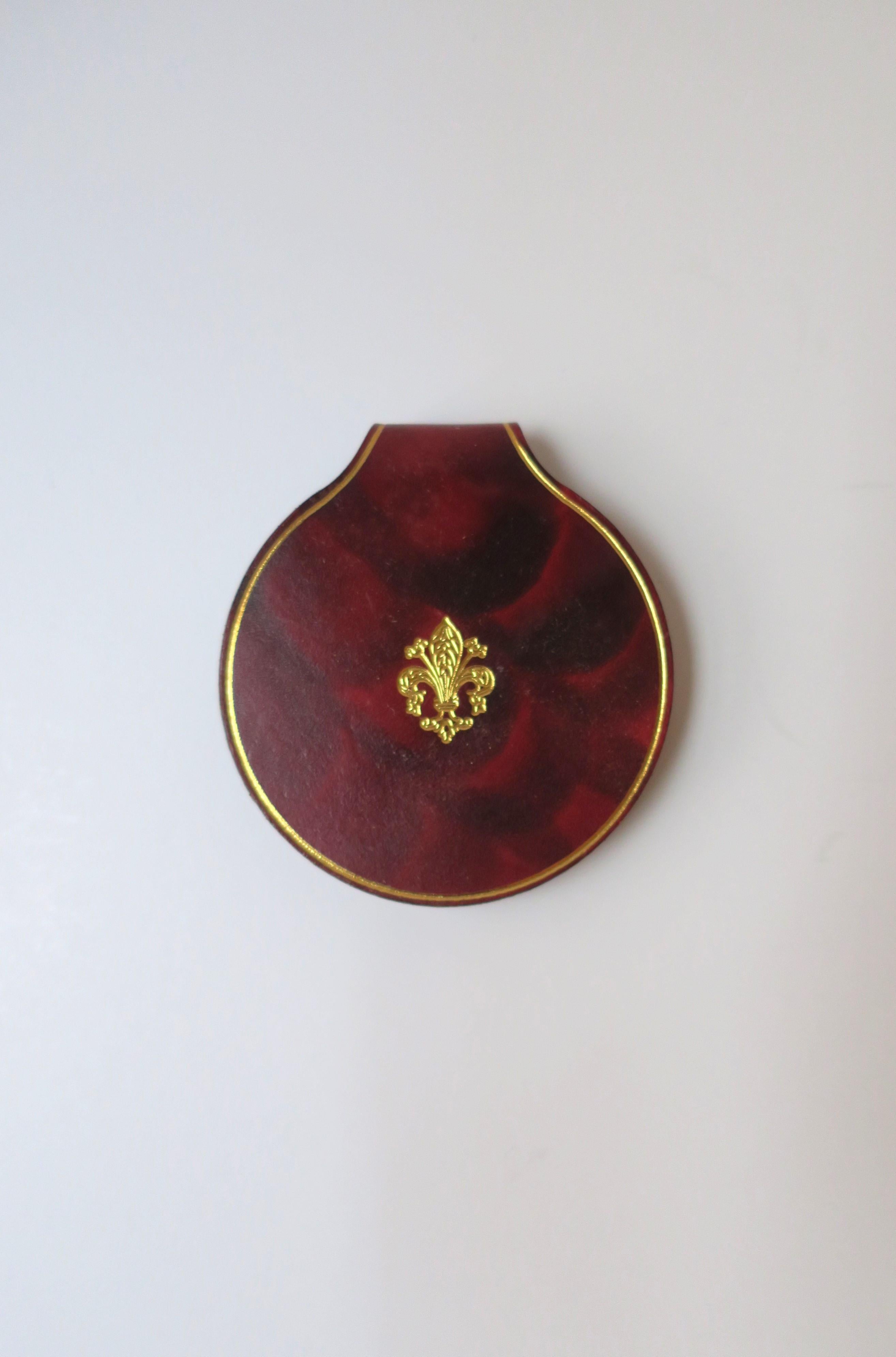 A beautiful Italian leather compact mirror with gold embossing, circa 20th century, Italy. This compact mirror is all leather in a red burgundy hue with gold embossing around edge, front center with fleur-de-lis design, inside around edge, and on