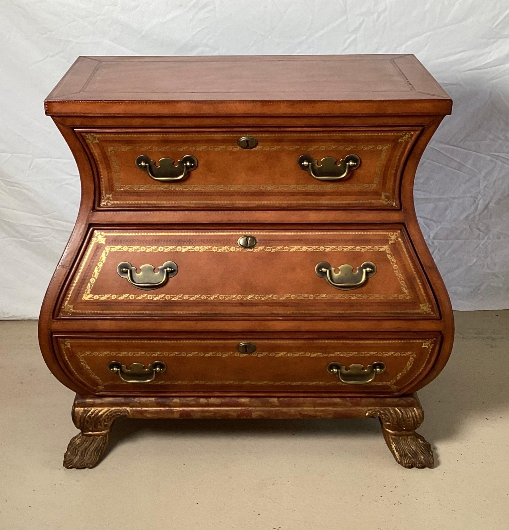 Handsome Leather Covered Bombe chest, made in Italy with brass handles. The medium caramel colored leather with gold tooling along the top and drawer fronts. The base is hand carved with an aged gilt wash to the surface. Very shapely and in