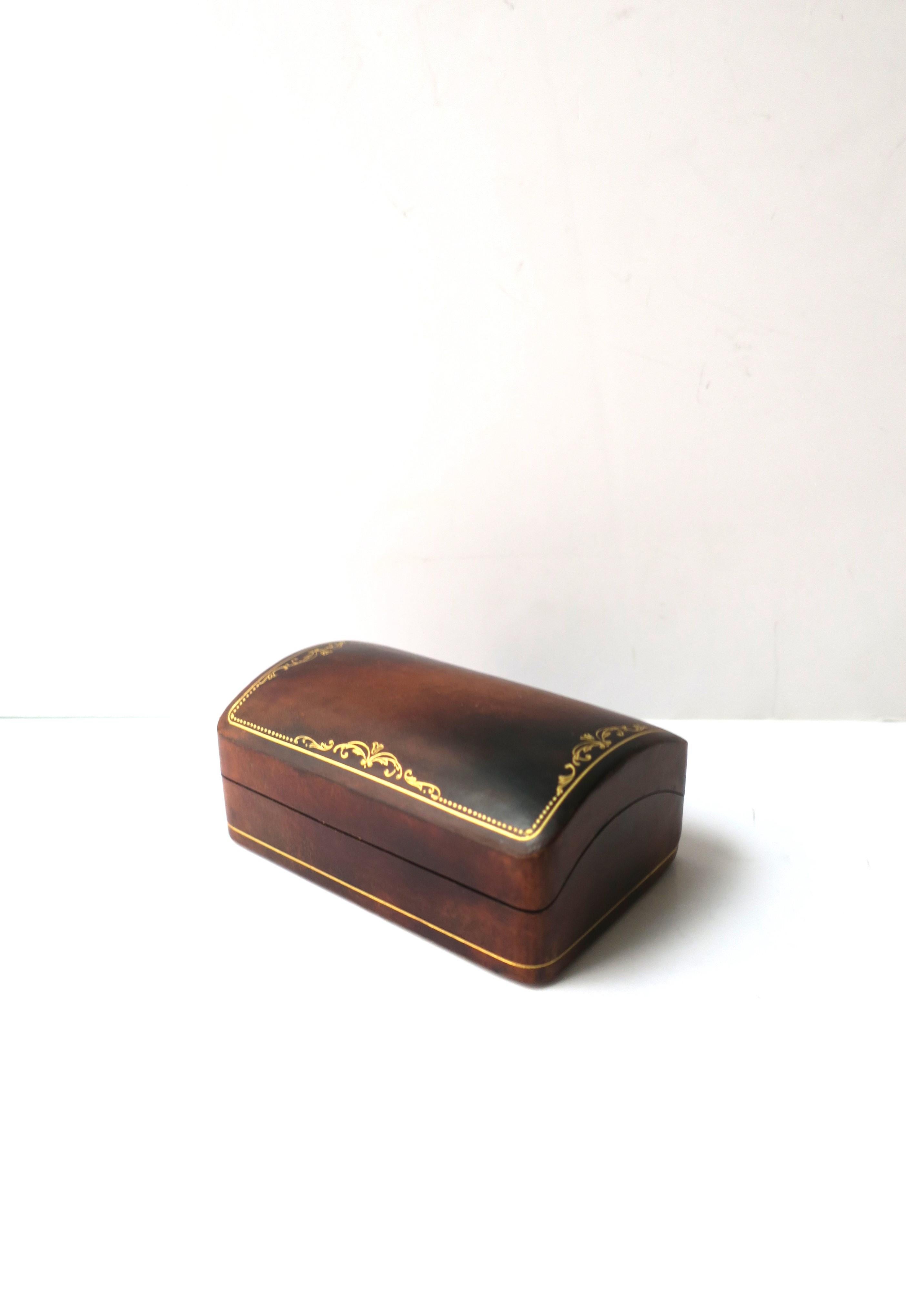 An Italian leather box with gold leaf tooling detail, circa mid-20th century, Italy. Leather is brown with gold tooling detail on top and around exterior edge. A great piece to hold jewelry (demonstrated) or small items on a desk, vanity area,