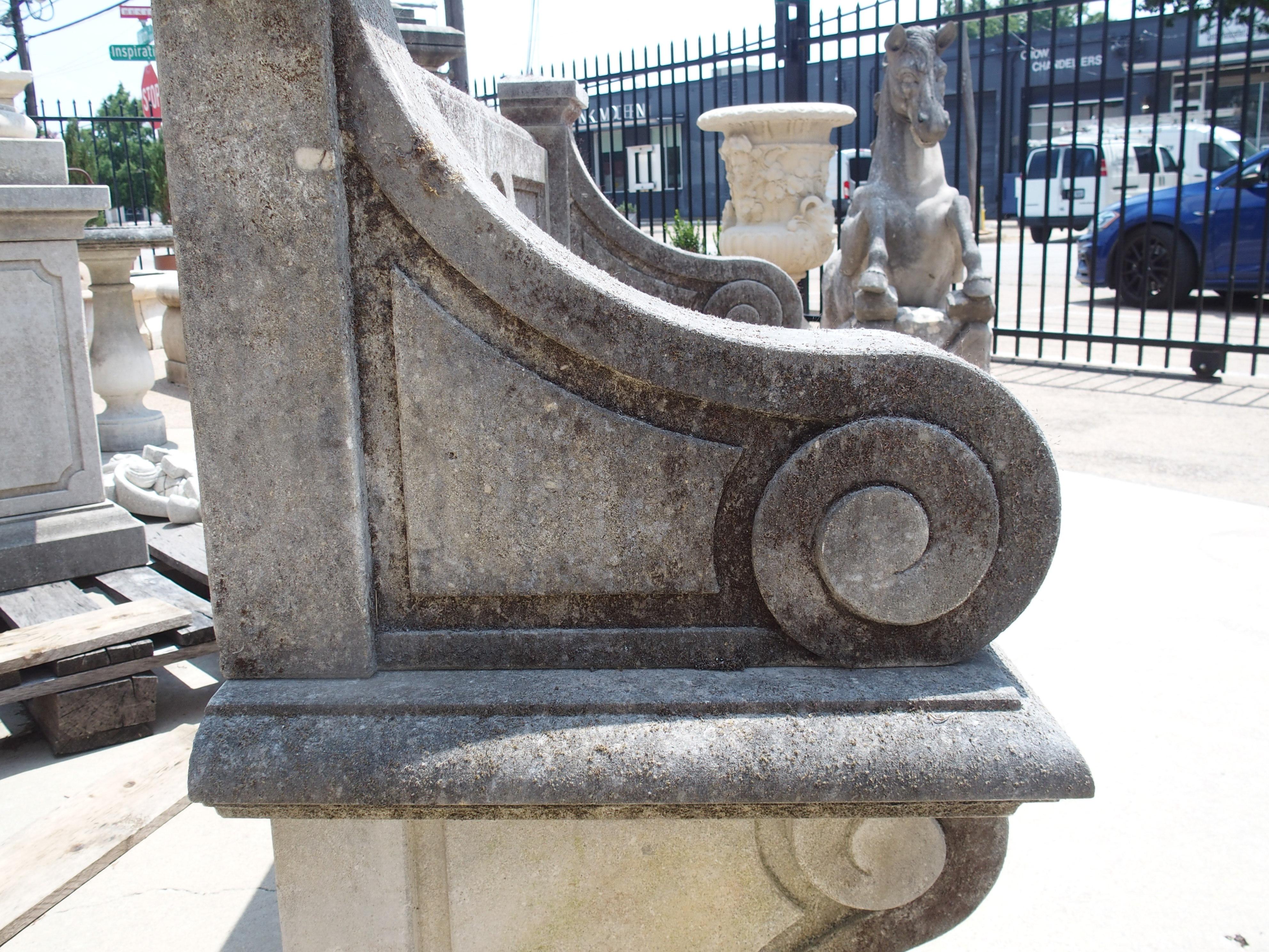 Sculpté à la main dans du calcaire italien, ce joli banc de jardin est orné d'une rosette sculptée dans le dossier de l'assise et de trois pieds fortement enroulés. Composé de neuf morceaux de pierre, le banc a une couleur gris pierre avec une