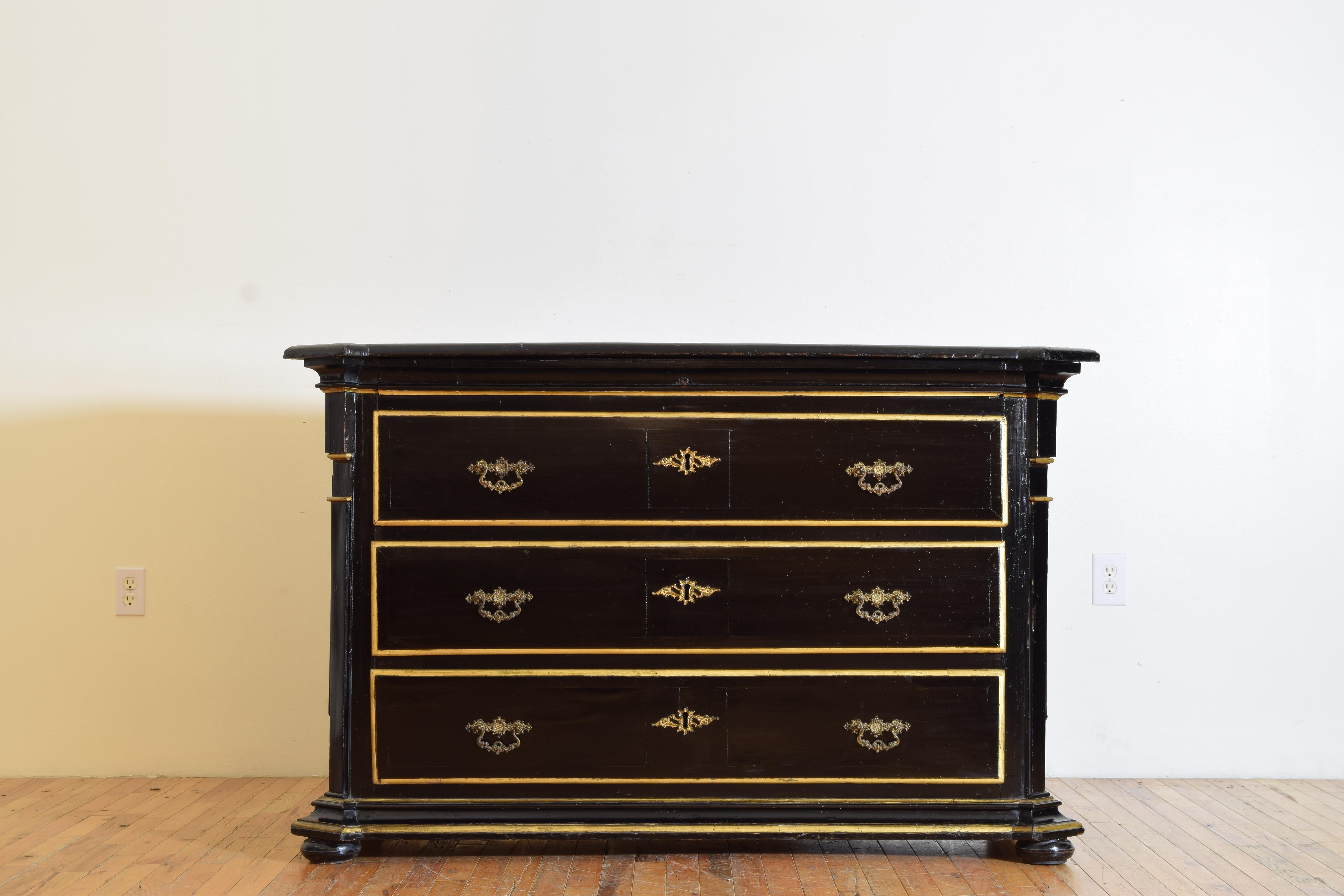 Constructed of ebonized walnut and having a rectangular top with notched and canted corners atop a conforming case housing three drawers all trimmed in gold leaf, the drawers retaining period brass handles, raised on flattened bun feet