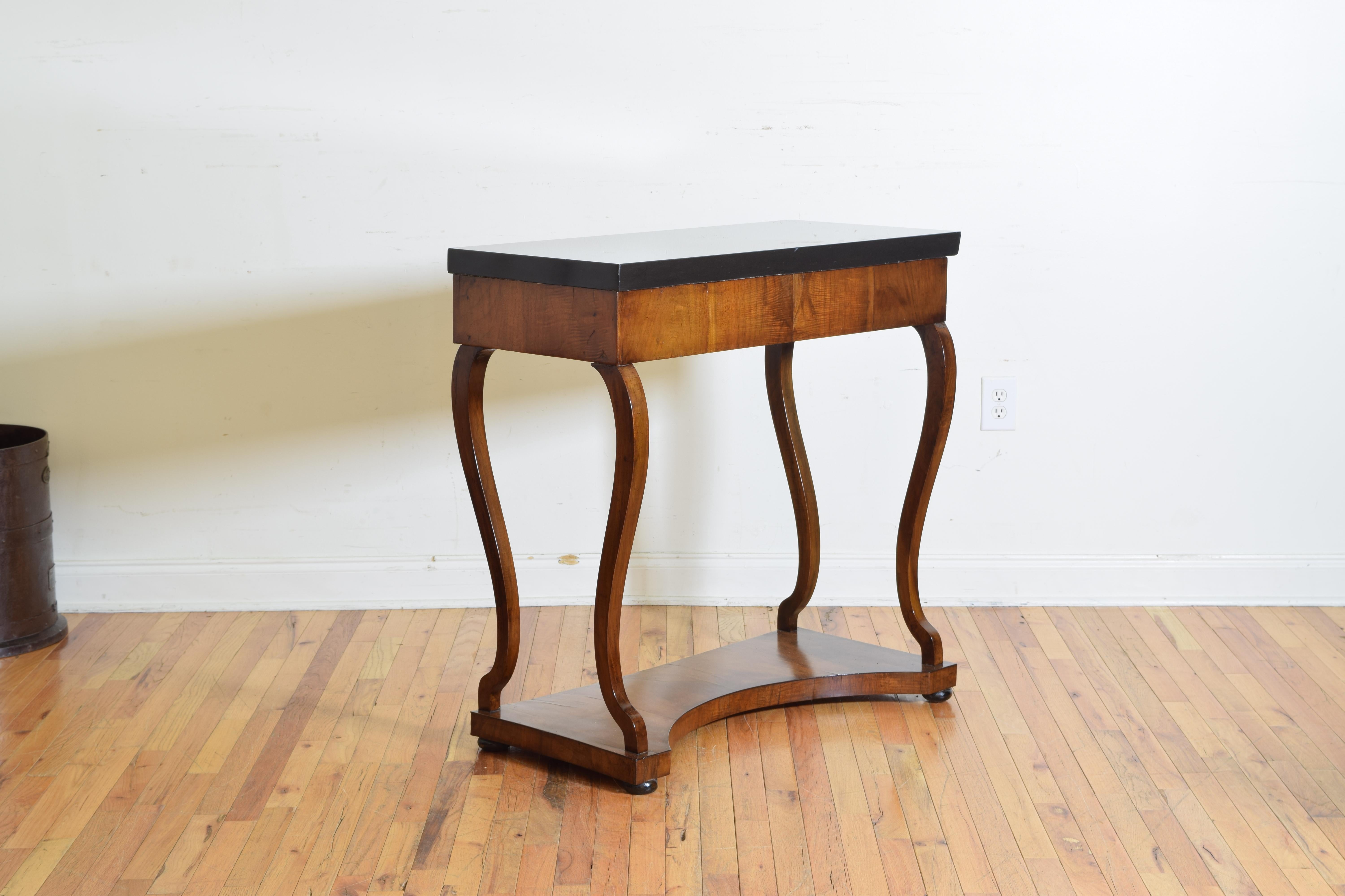 Having a thick nearly black top resting upon a console table covered in walnut veneer, the simple apron supported by elegantly shaped legs that flare near the bottom where they attach to the lower plinth which is raised on small ebonized bun feet.