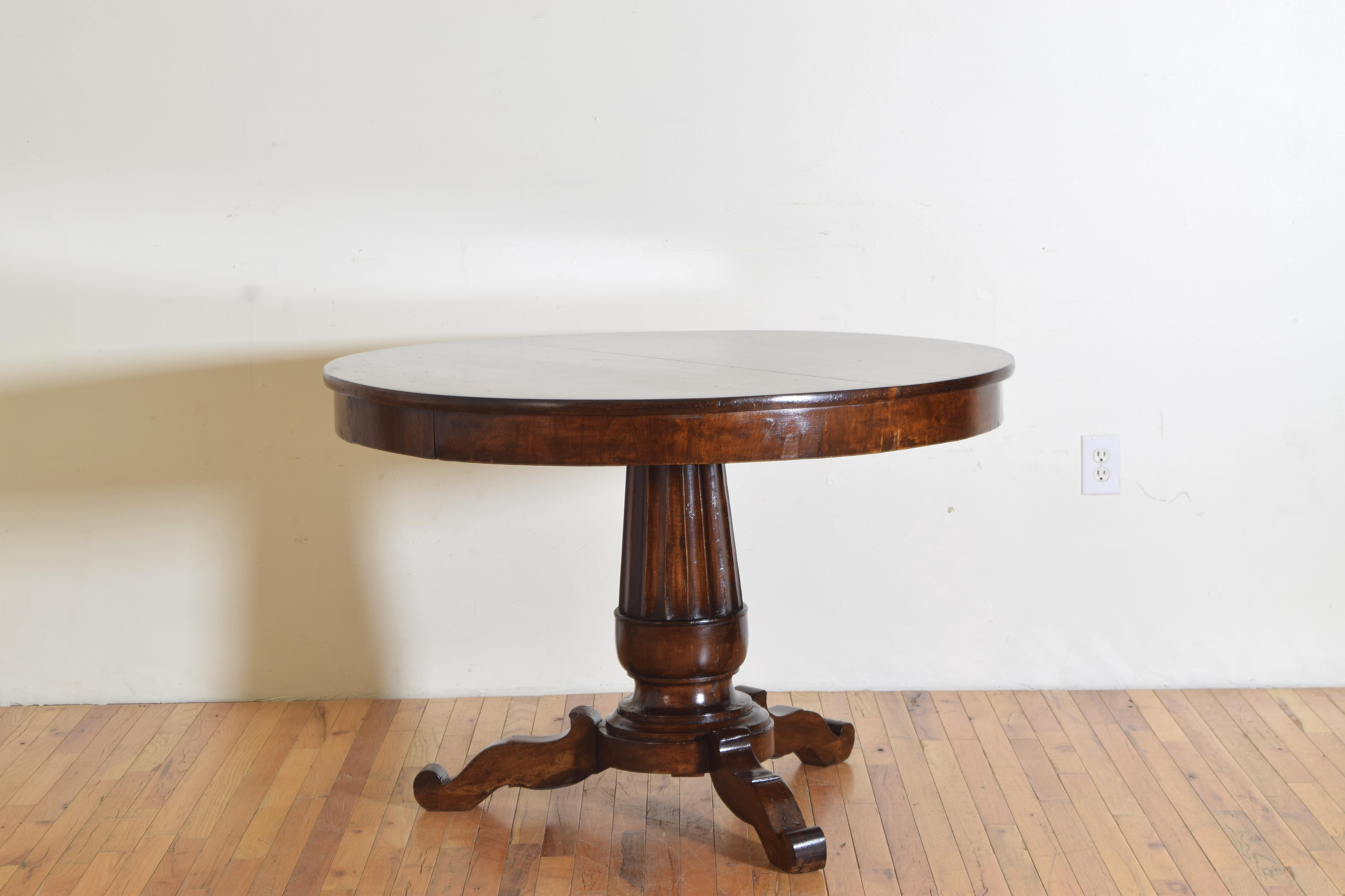 Having a circular solid walnut top resting upon an apron which is veneered and houses two opposing drawers, the top is raised on a tapering fluted column terminating in a stepped tripartite base issuing three shaped legs with upturned feet.
