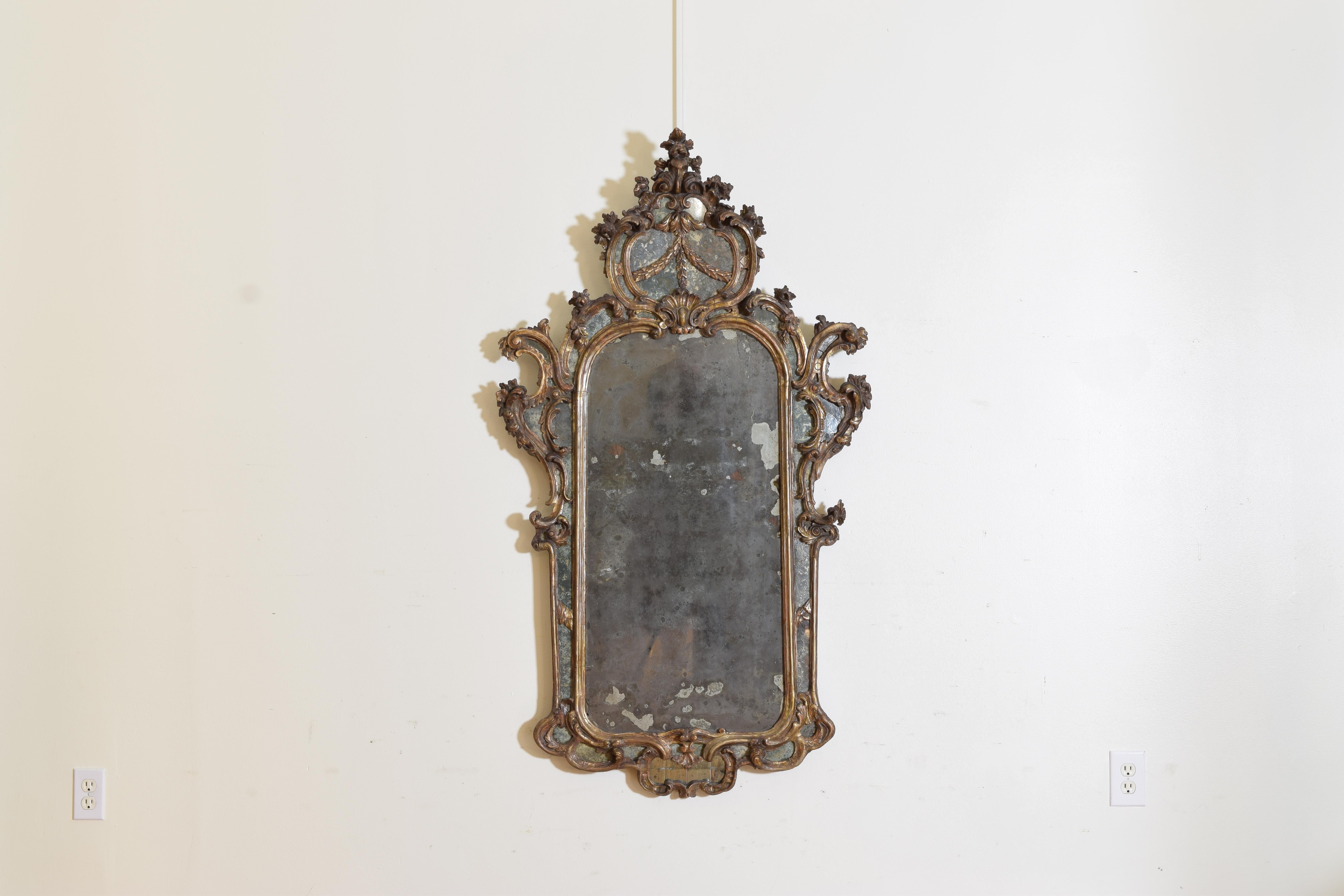 The original mirror plate of silvered mercury glass surmounted by a giltwood frame consisting of varying scrolls and leaf-forms the upper middle with a shell carving below carved garland roping