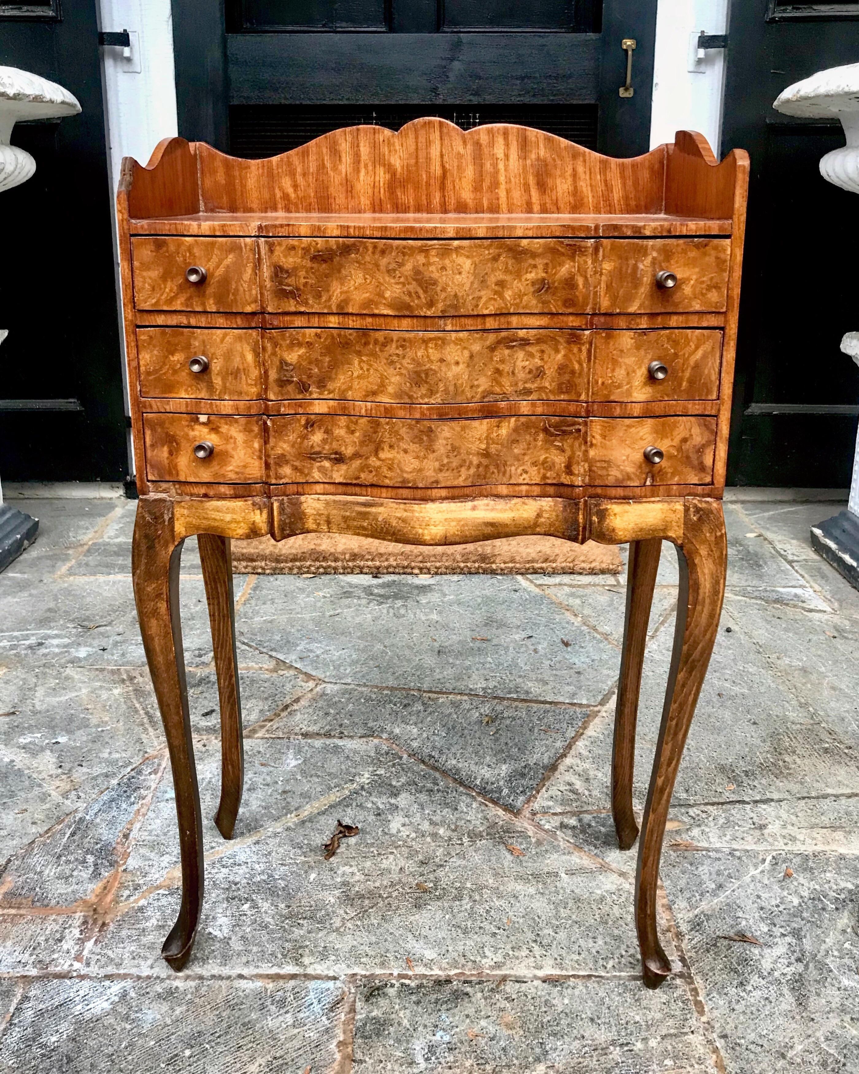 A good looking Louis XV style cabinet having three serpentine shaped thin drawers residing over dramatic and thin cabriole legs, circa 1955, the nightstand adds warmth and dramatic flare with the classic and rich look of burl wood veneer. Great