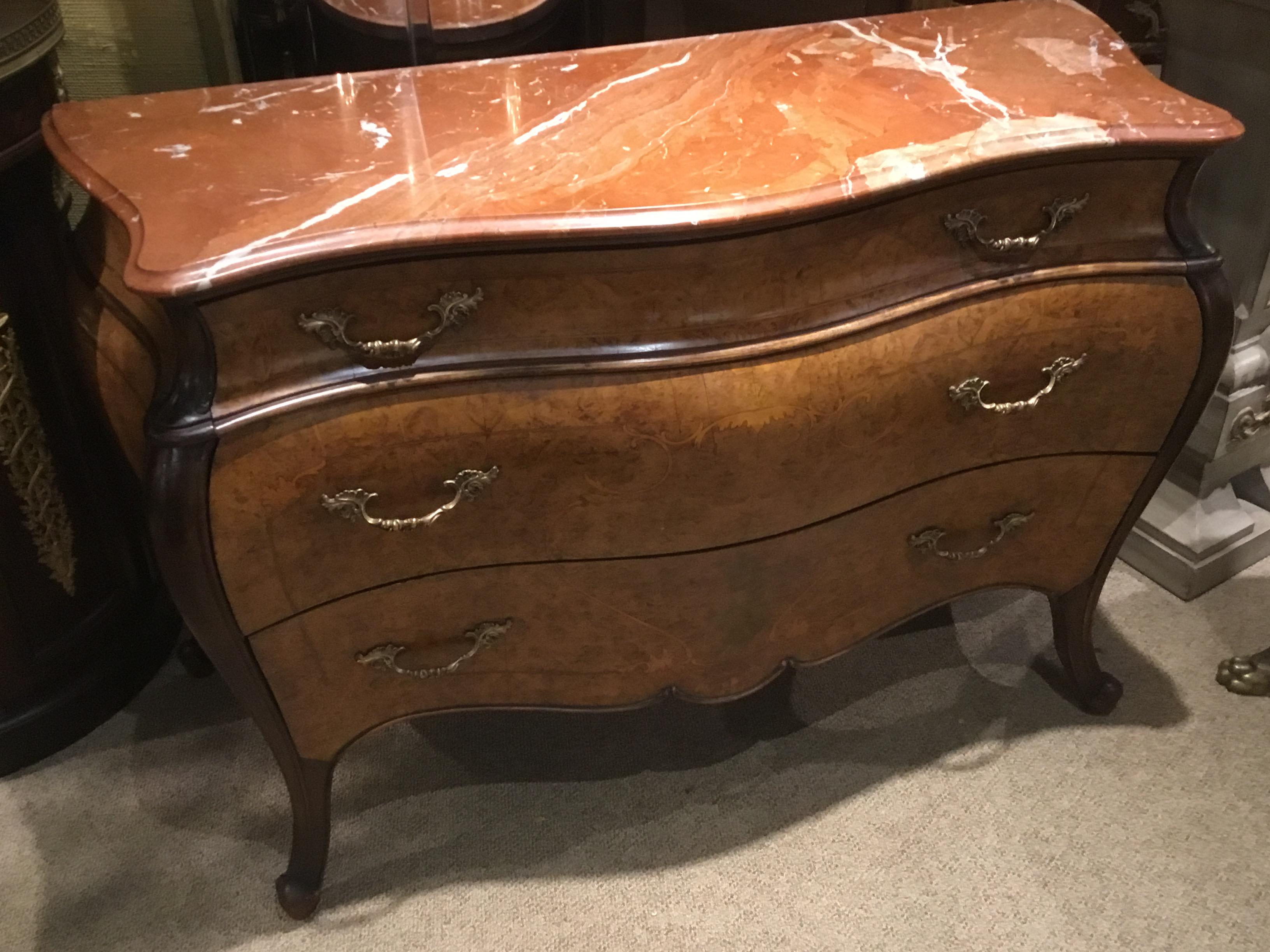 Handsome bombe’ form commode in a burl wood case fitted with three drawers and
accented with scrolled marquetry rising on curled feet.