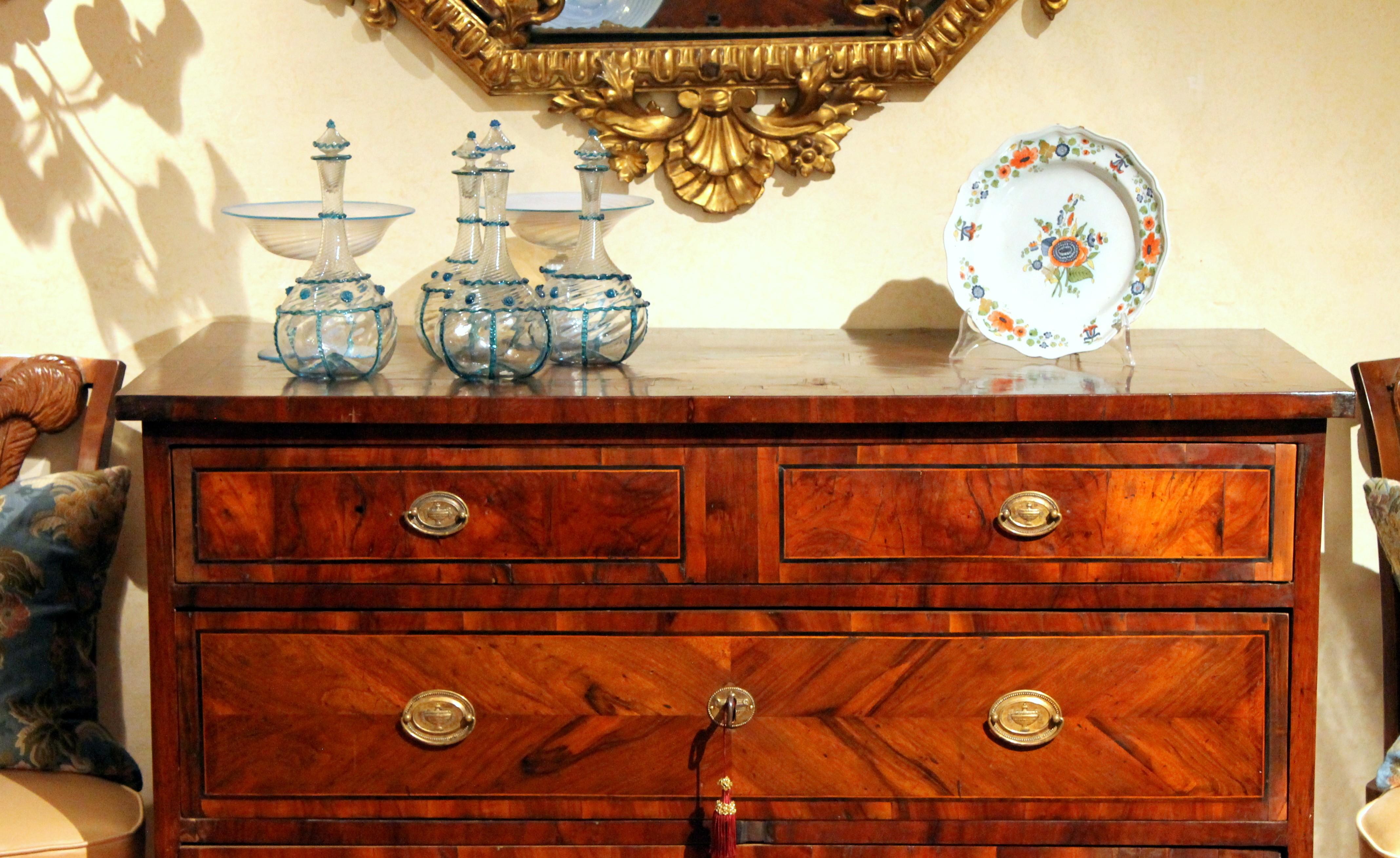This Italian Louis XVI period walnut three-drawers commode from the late 18th century, with bronze handles, banded drawers and fluted tapered square legs stands out for its marquetry, a wonderful hand crafted inlay work that adorn both the top and