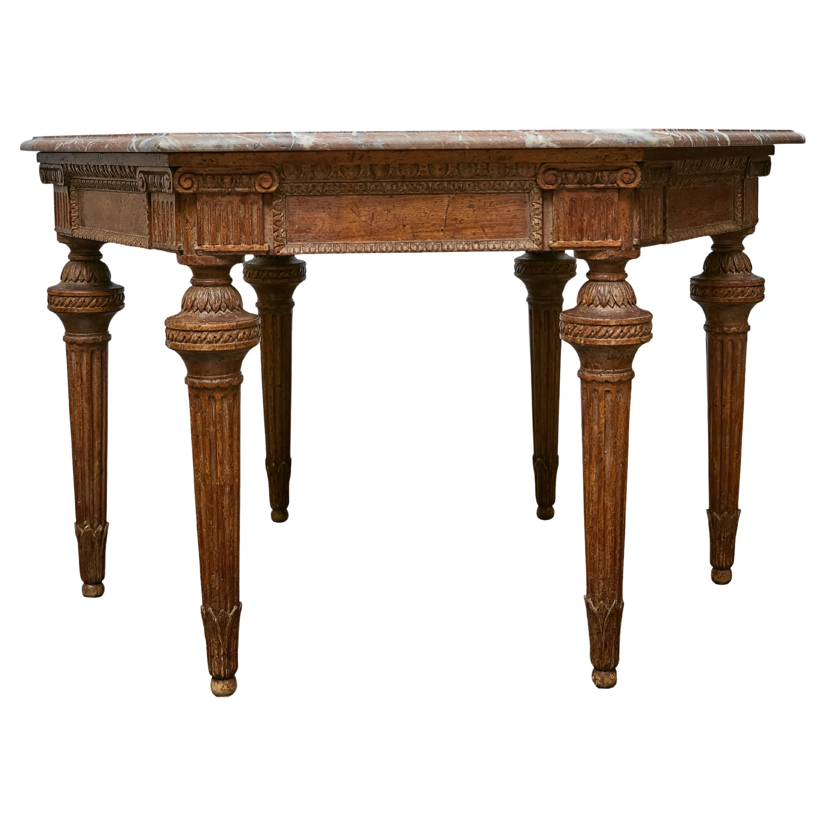 This Italian carved walnut table presents an uncommon hexagonal silhouette topped with a substantial slab of variegated marble, a combination that immediately sets it apart from standard 19th-century forms. The base shows the disciplined vocabulary