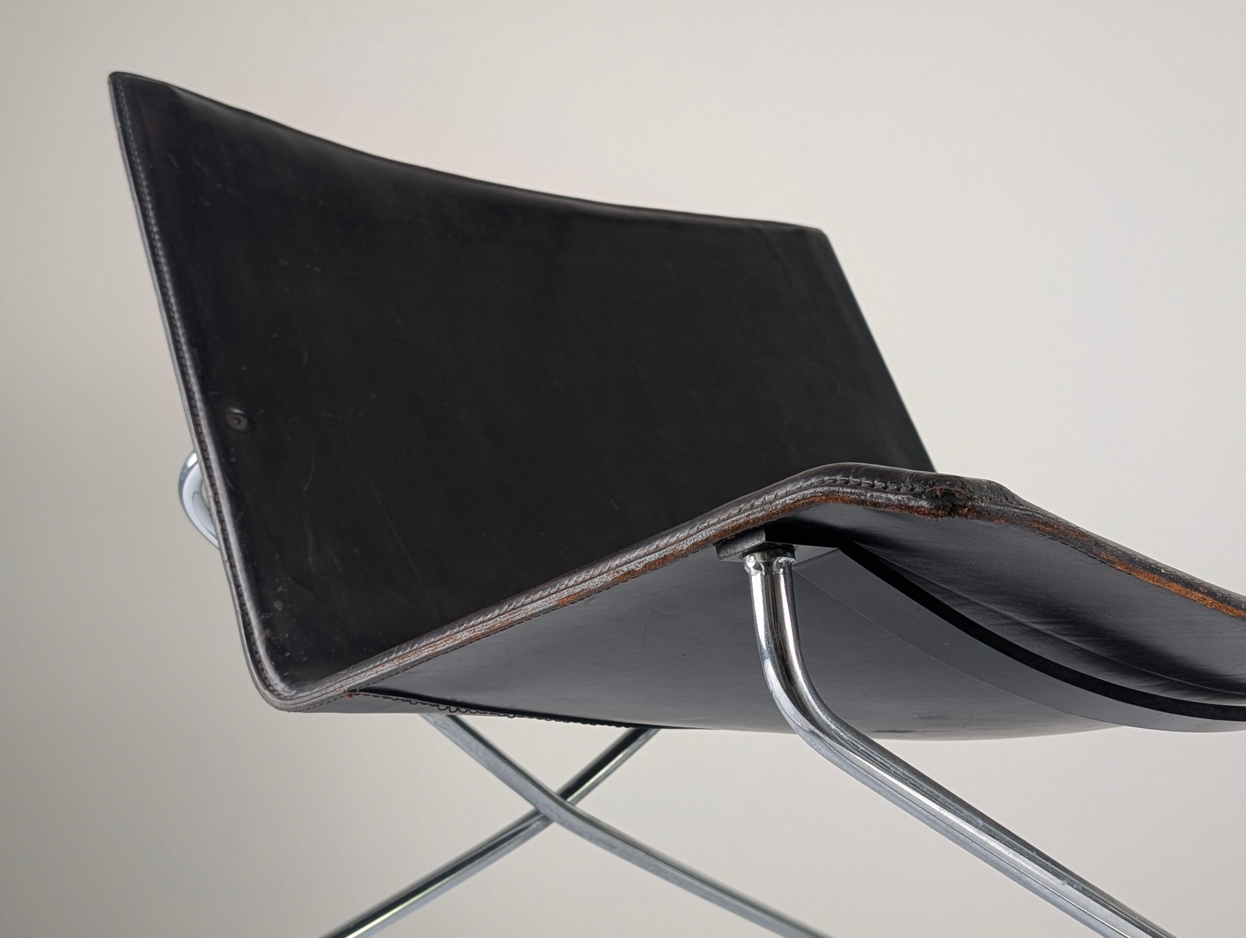 Low Italian lounge chair from the 1980s featuring a bent chrome tubular structure supporting a continuous black leather seat. Its minimalist X-frame offers sculptural elegance and timeless appeal, while the leather shows an original patina with