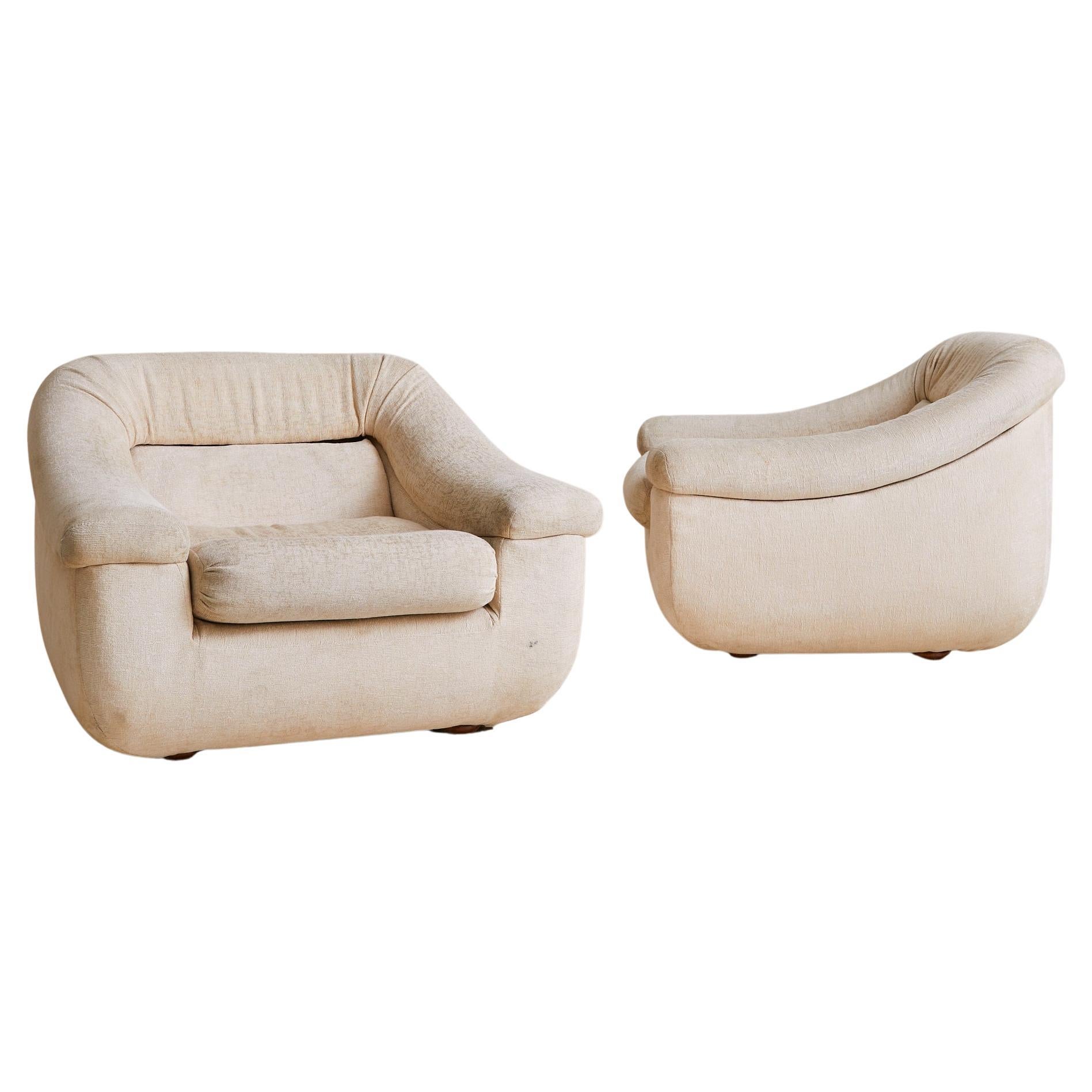 Sold and priced individually.

A generously proportioned Italian lounge chair from the 1970s, upholstered in its original ivory-toned fabric. The silhouette is softly contoured, with deep, rounded arms that flow seamlessly into a low, enveloping