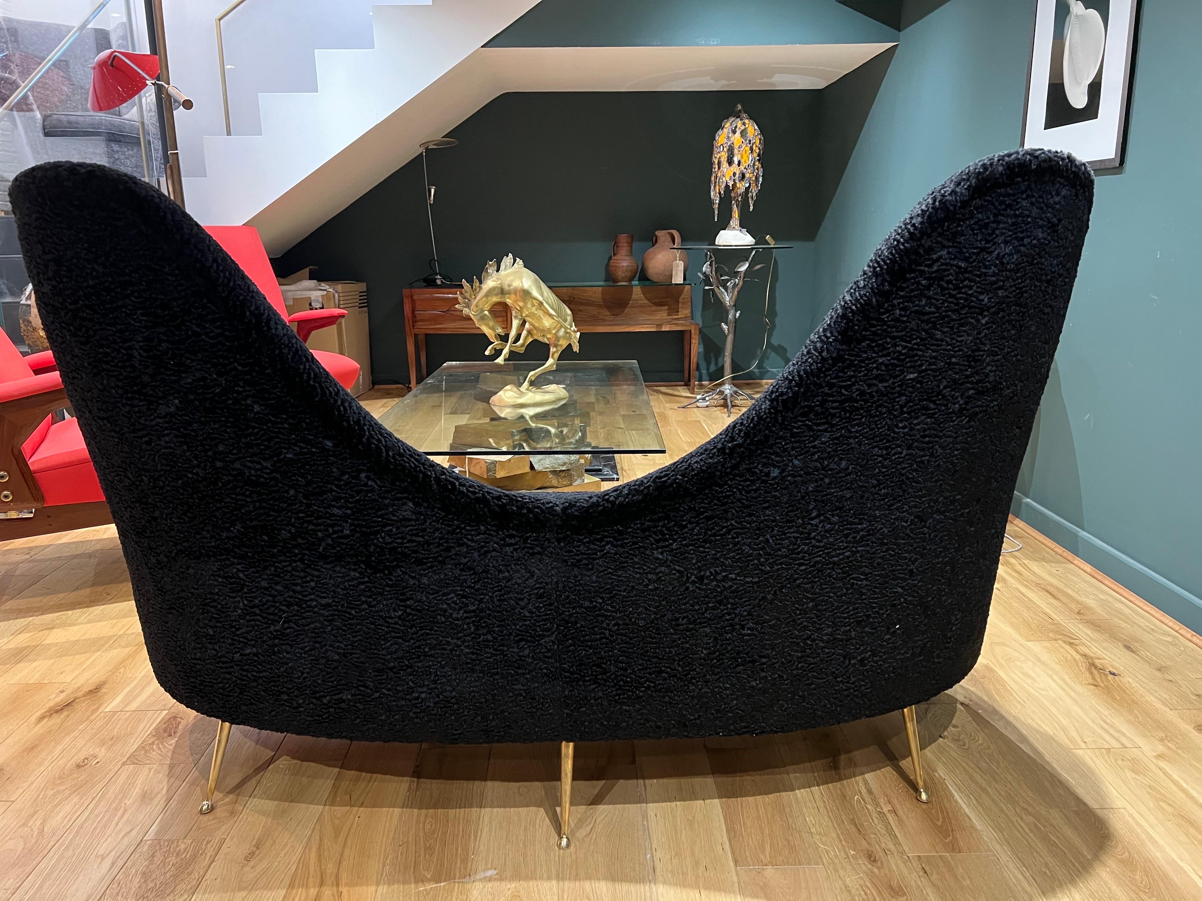 An Italian kidney shaped love seat upholstered in buttoned black wool boucle. The sofa has two brass feet to the front and three to the rear . An organic design that will be a great addition to any room environment.