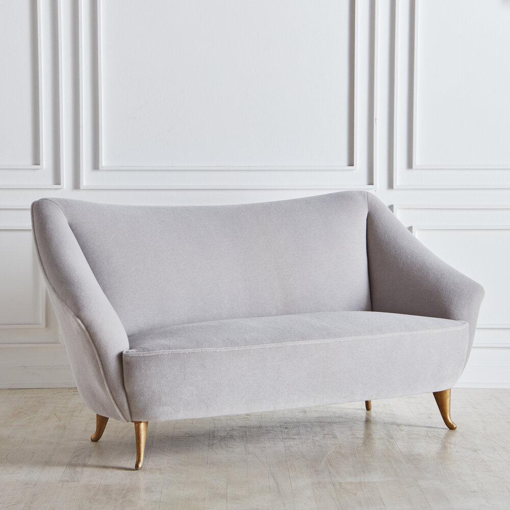 A two-seat settee newly reupholstered in a gorgeous light gray Italian mohair. Featuring tapered brass legs and a sculptural curved wingback shape. This piece is in the style of other works by Gio Ponti manufactured by Isa Bergamo in the 1950s.