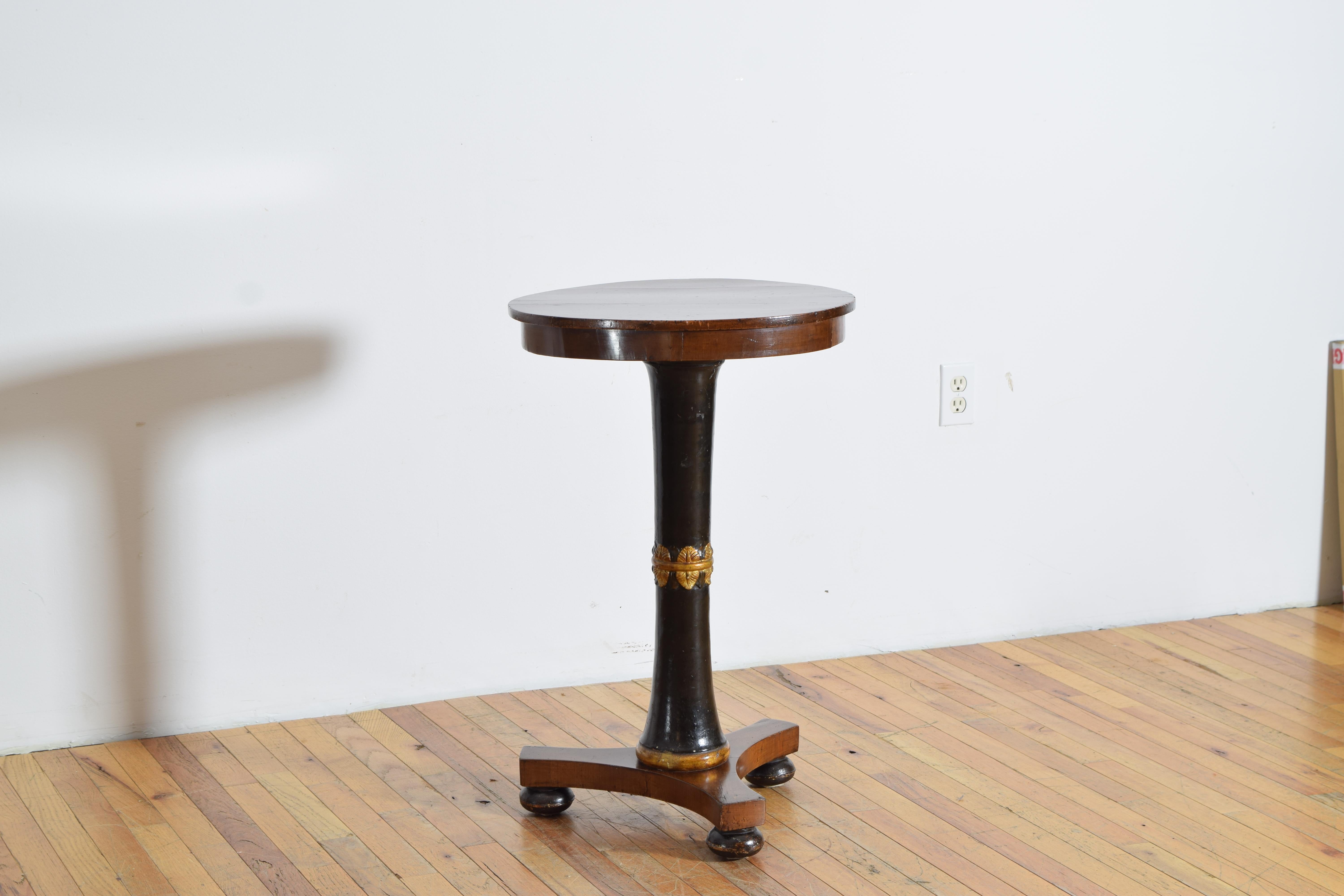 having a walnut circular top with above a conforming apron raised on a slightly hourglassed ebonized standard surmounted by a ring of gilded acanthus leaves, the bottom of the standard having a rounded gilded ring above a tripartite base raised on