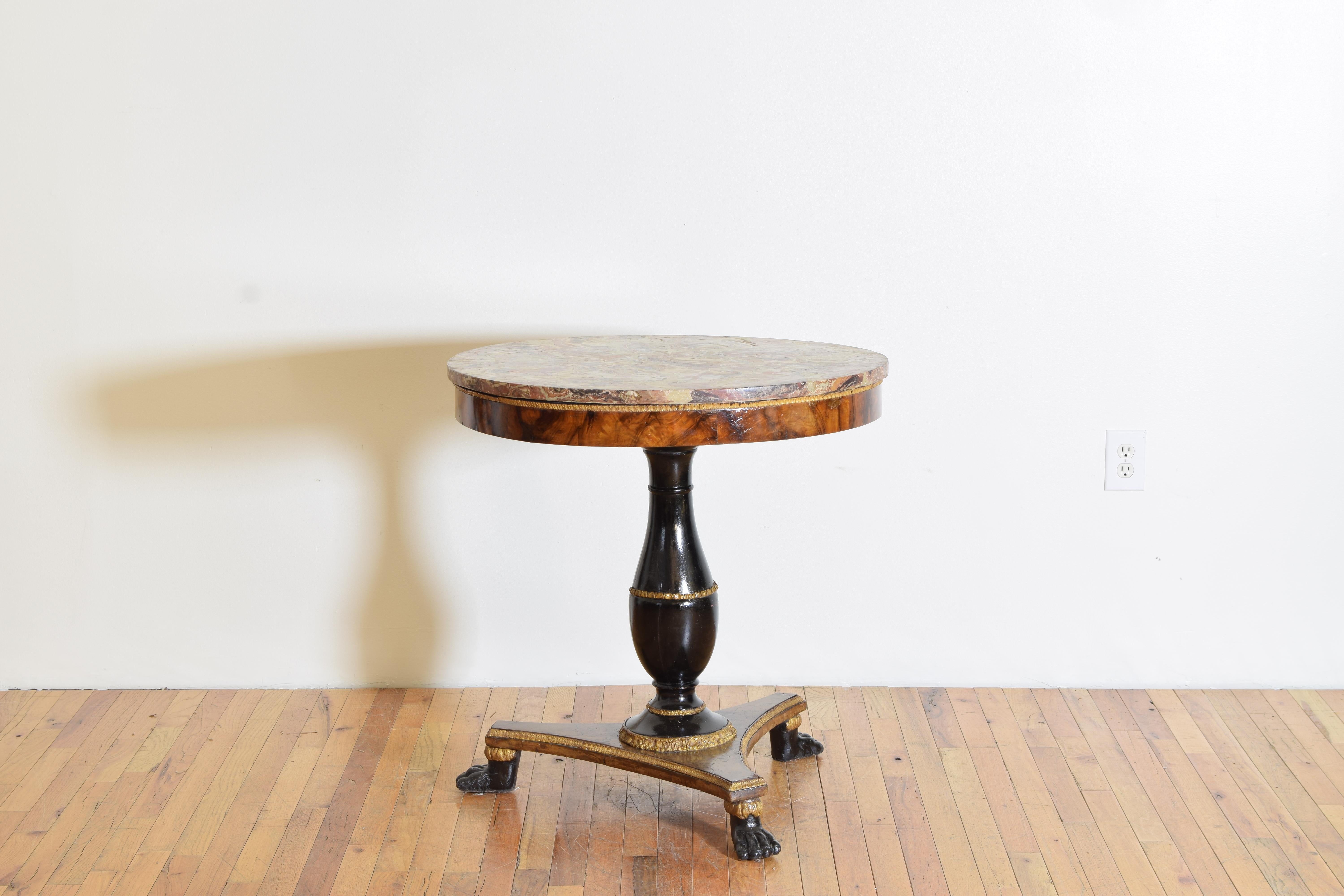 Having a circular hand painted scagliola top resting atop a circular frame, the thick walnut veneer of a lovely grain, the ebonized columnar standard with a carved giltwood ring resting upon a walnut veneered tripartite base raised on giltwood paw