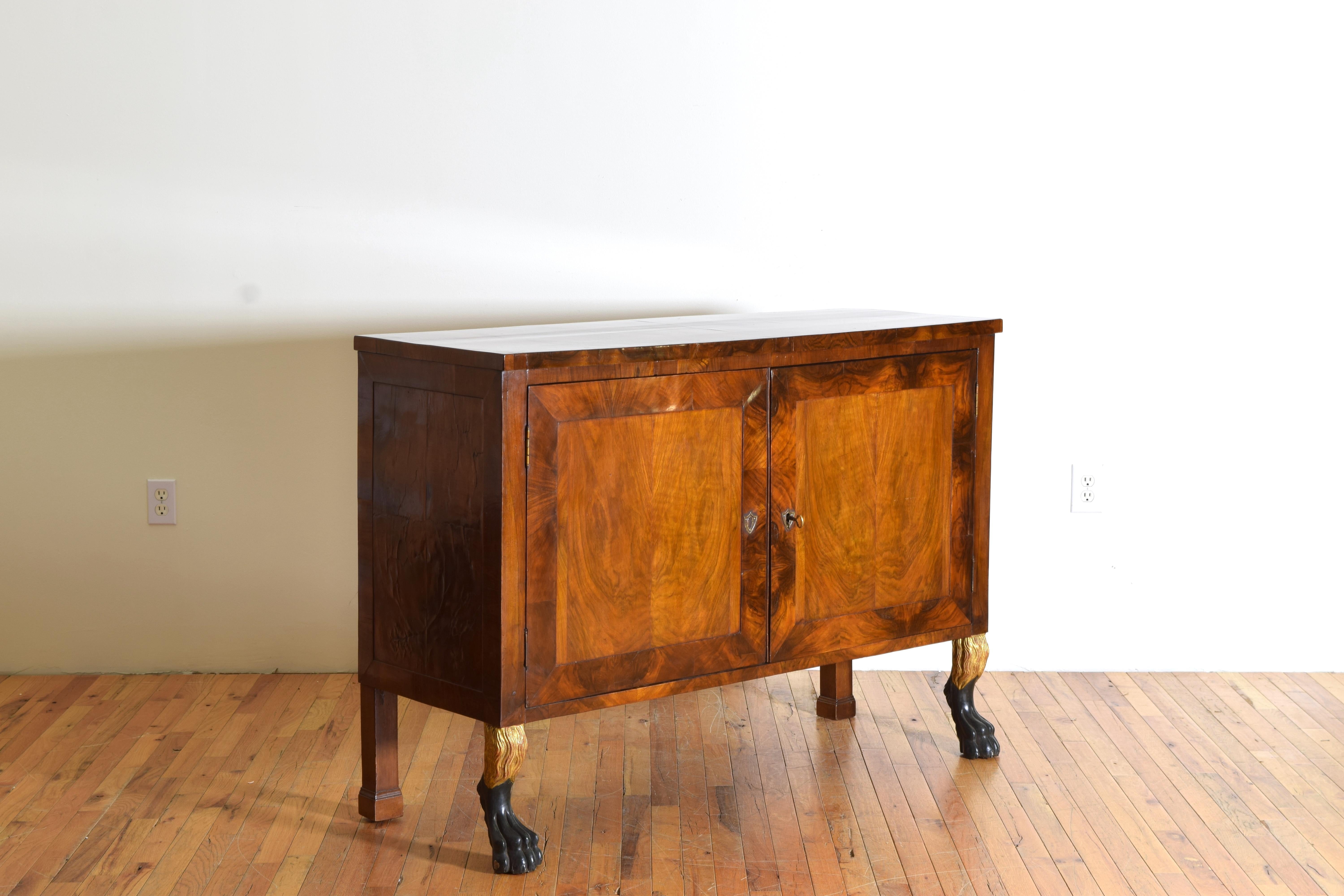Having a rectangular top above a conforming case with two paneled doors, the interior fitted with drawers and shelving, the feet are ebonized carved paws with carved giltwood legs