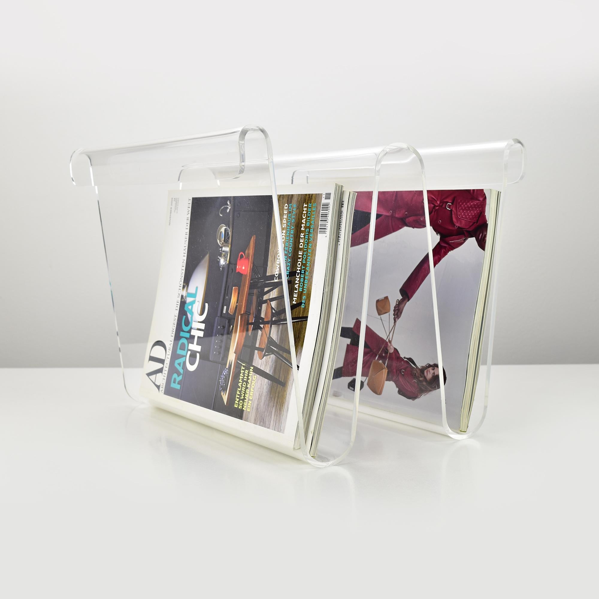 A wave-shaped magazine holder which also can be used upside-down, made of transparent Plexiglas or acrylic in the style of Guzzini. 

This elegant piece seamlessly integrates into a modern decor, adding a touch of sophistication and contemporary