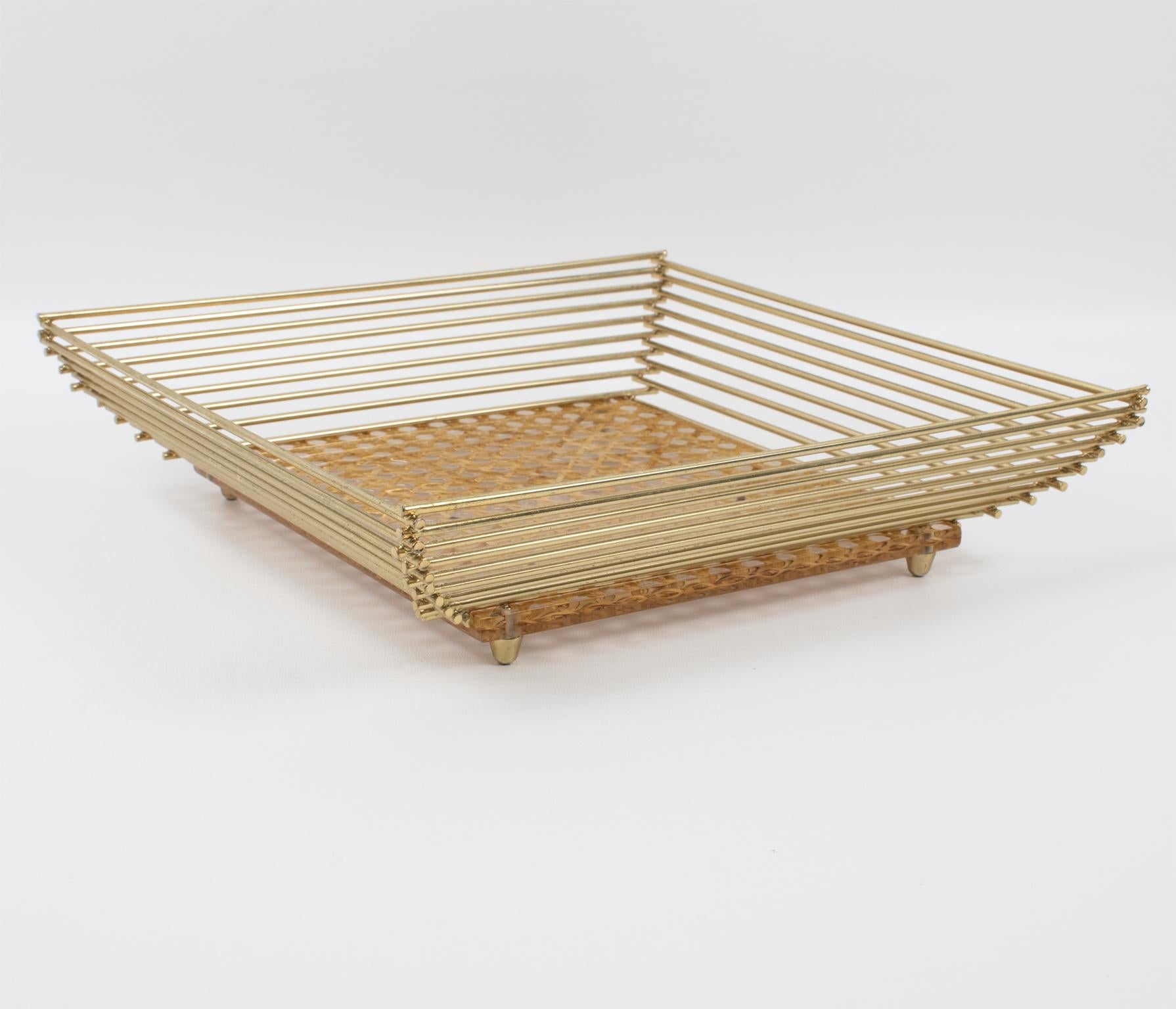 This stunning barware serving tray was crafted in Italy circa 1970. The rare platter or decorative bowl boasts a square shape with a raised gilded brass all-around gallery and genuine rattan or wicker embedded in the Lucite base. This tray is