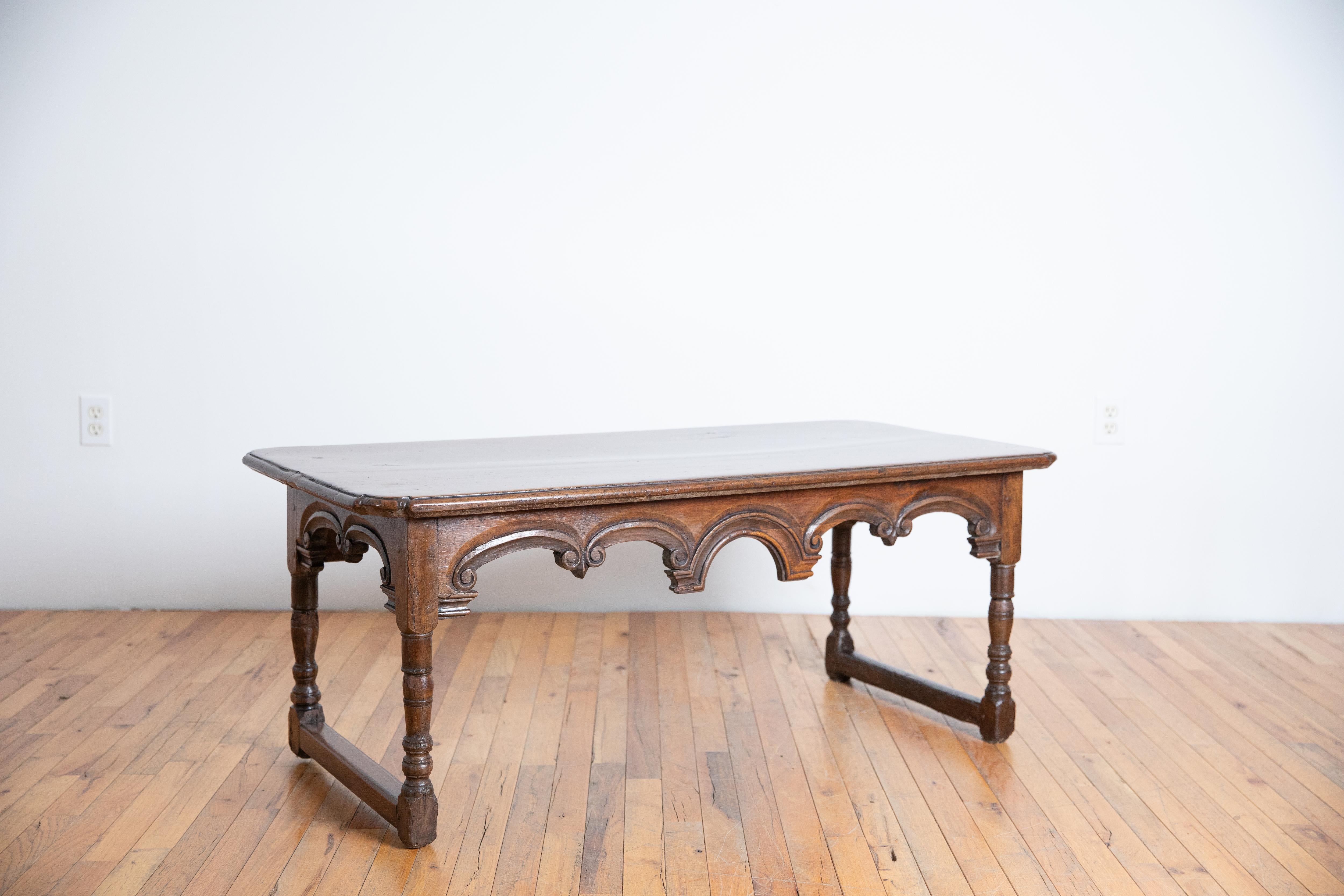 Le plateau rectangulaire aux angles arrondis est surmonté d'un cadre avec des tabliers sculptés en forme de volutes et d'arcs centrés, le cadre reposant sur des pieds tournés reliés par deux brancards, cette table a été réduite en hauteur.