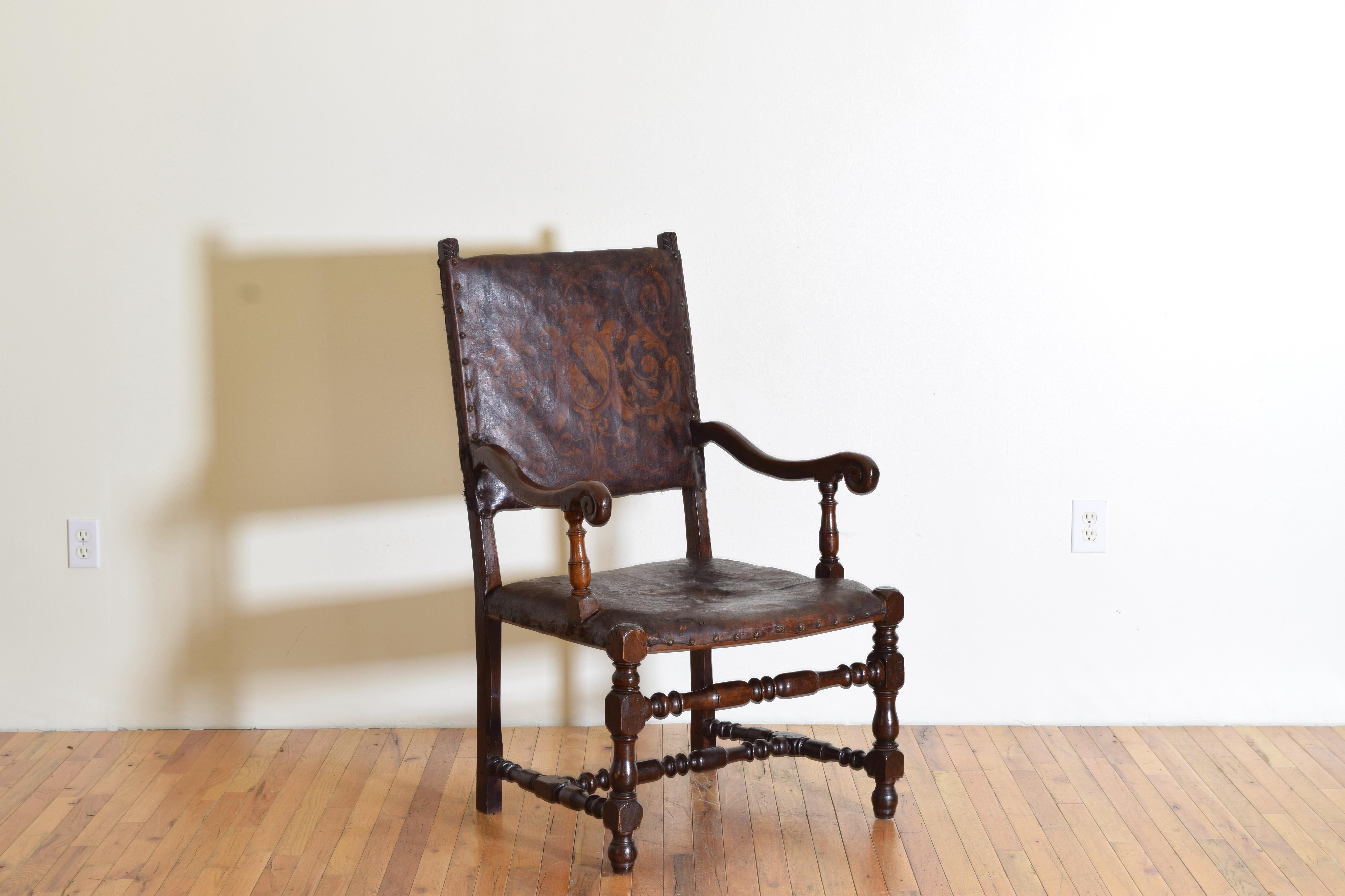 having a rectangular backrest with small carved finials and a fitted seat, the arms recessed, turne arm supports, legs, and stretchers, raised on turned feet, the upholstery is a tooled and polychrome painted leather with a stemma pf the Calleri