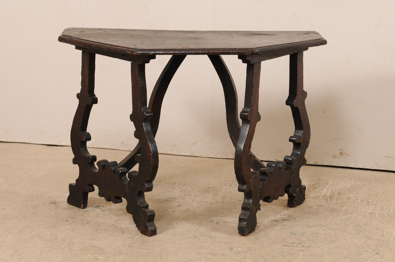 An Italian walnut table from the turn of the 17th-18th century. This antique table from Italy features a demi-style halved-octagon shaped top which is raised upon a pair of sinuously carved and canted lyre-legs. The lyre legs are braced with two