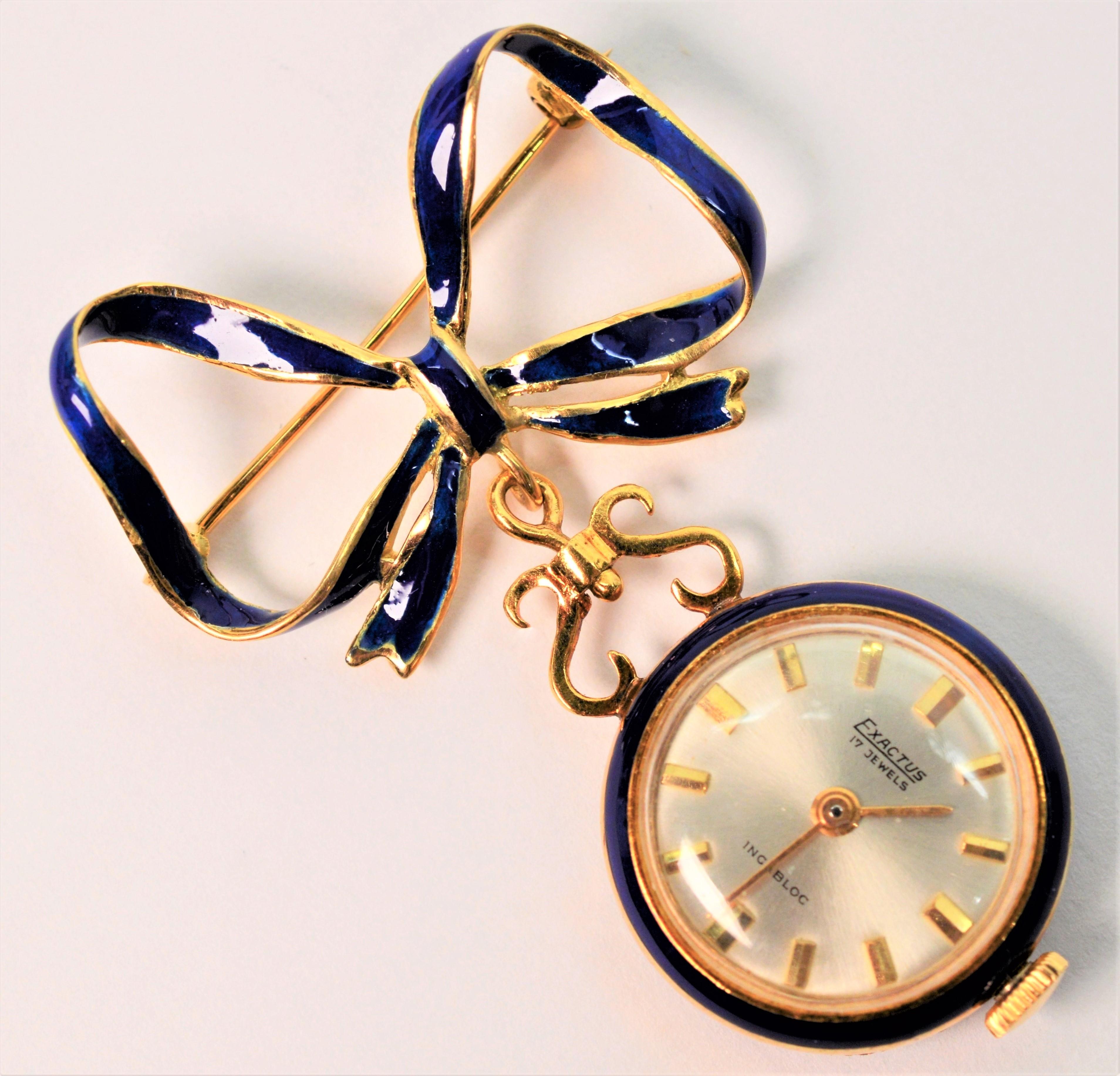 Diese in Italien gefertigte Brosche mit romantischem Charme beginnt mit einer zart gebundenen Schleife aus vierzehn Karat Gelbgold mit einem mittleren Band aus kobaltblauem Email. Ein runder 20,72 mm (3/4 Zoll) großer, goldener Uhrenbügel ist an der