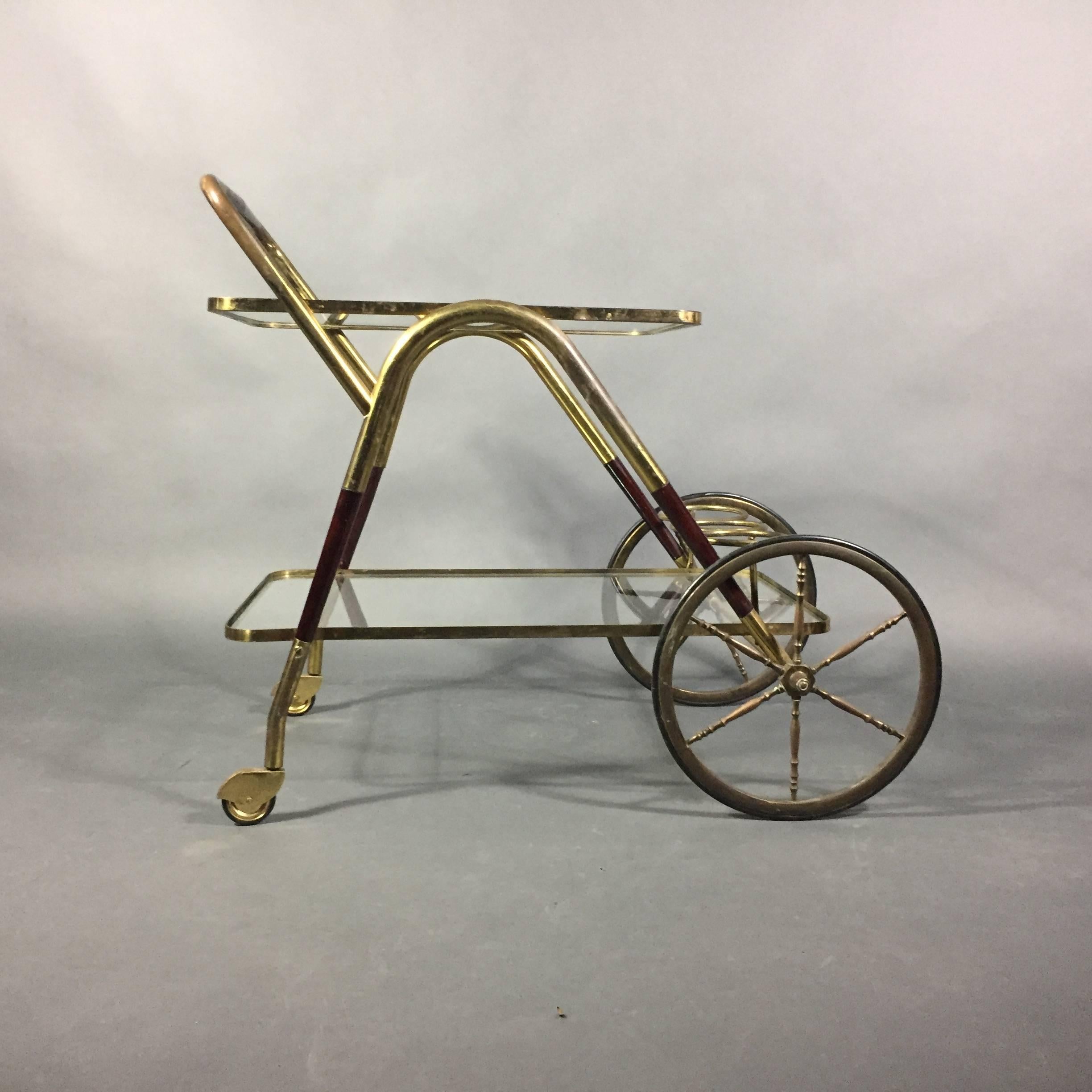 Classic Mid-Century Modern Italian drinks cart from the late 1950s or early 1960s that is perfect apartment size with a small glass top over lower full-glass shelf containing three bottle holders. Frame is in brass with portions designed in carved