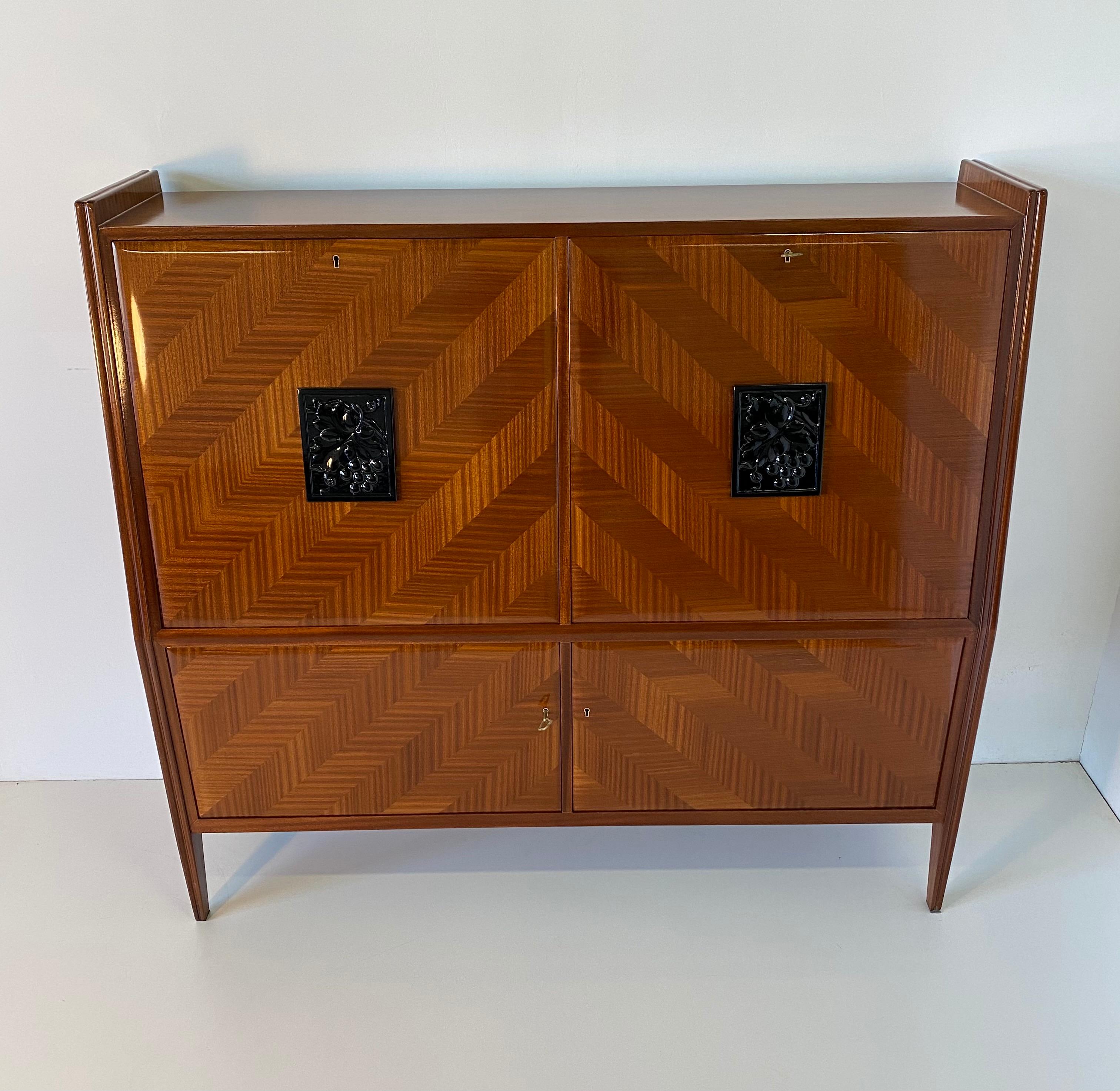 Precious cabinet secretaire produced in Italy in the 1950s,
The whole cabinet is veneered in mahogany with a fine solid wood carving in the center of the two doors representing two bunches of grapes.
The interiors are in maple.
Completely restored