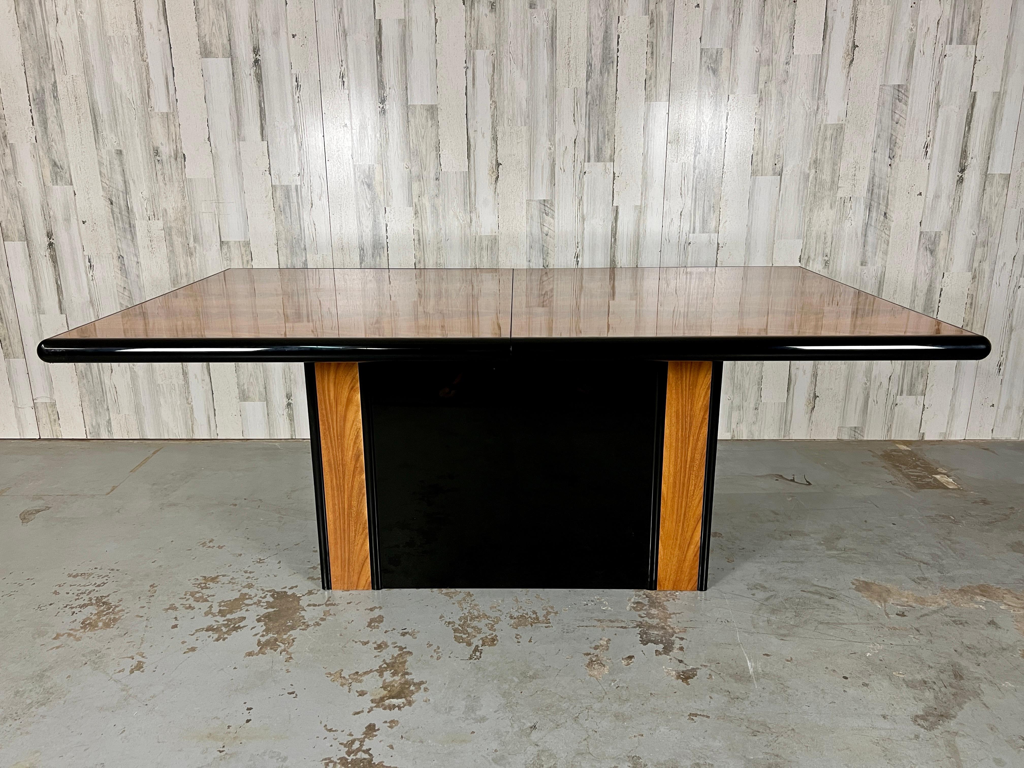 Italian mahogany & lacquer dining table. This table top stands on a black lacquer and wood accented pedestal. One leaf extends this table out to fit up to 10 dining chairs (depending on chair size).